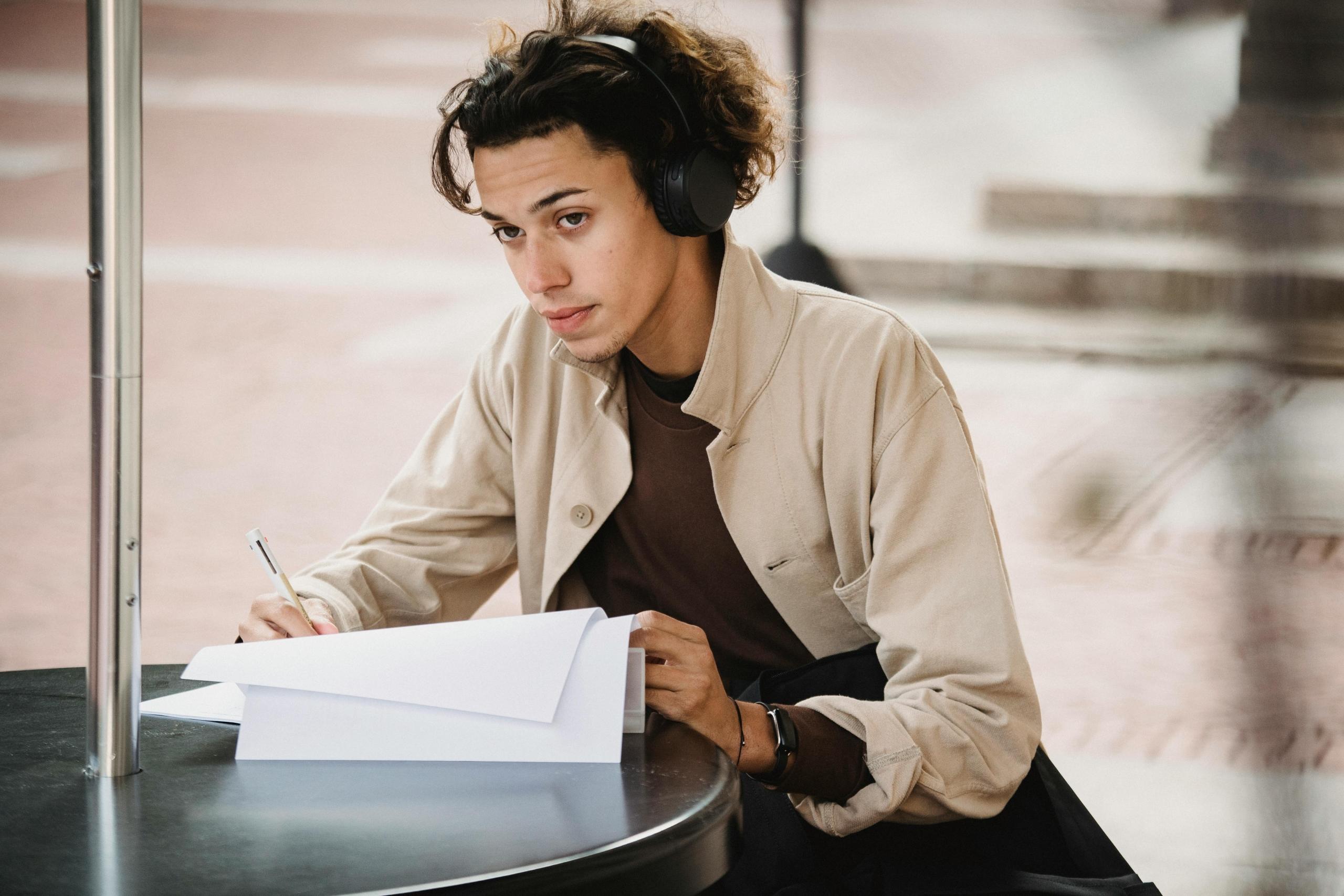 young adult wearing headphones and studying at a table