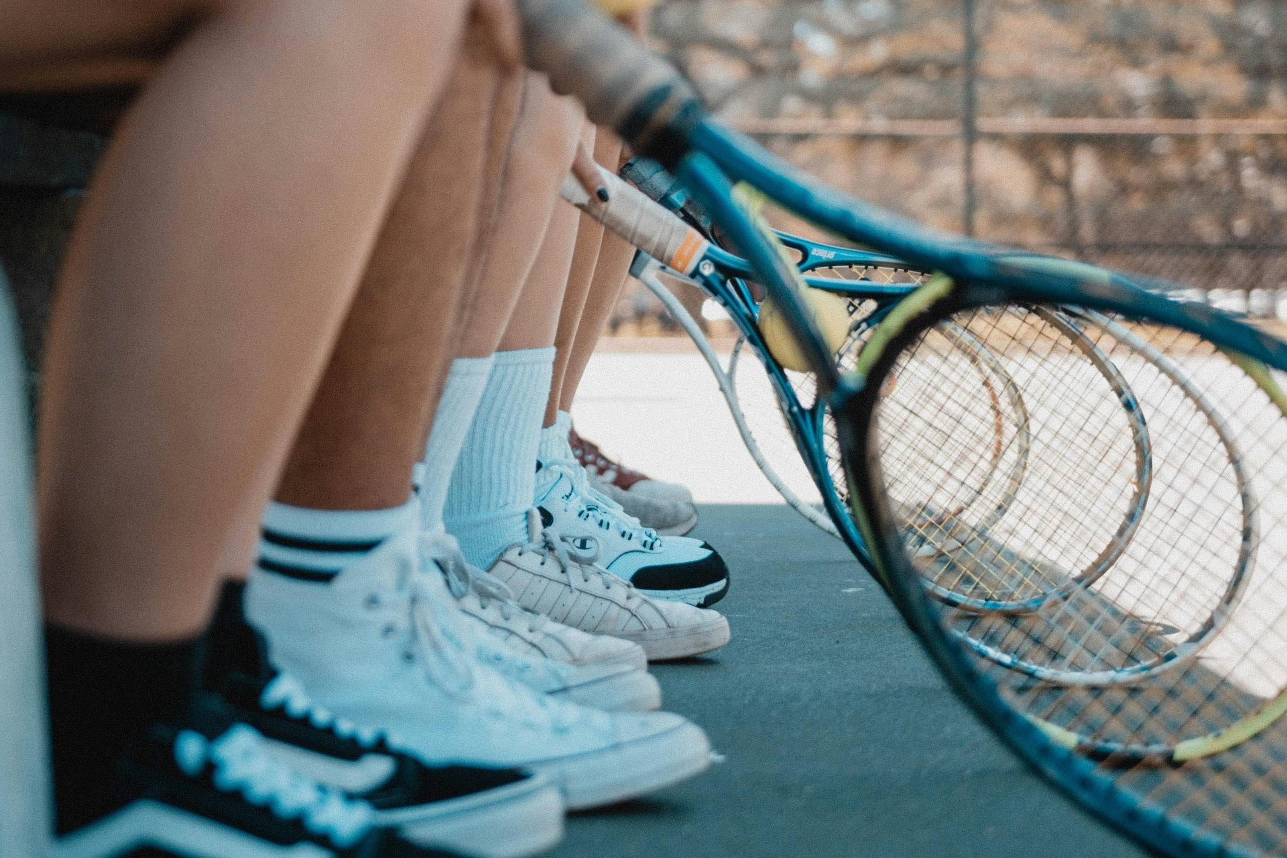 close up of the legs of tennis players sitting down with their tennis rackets outstretched in front of them
