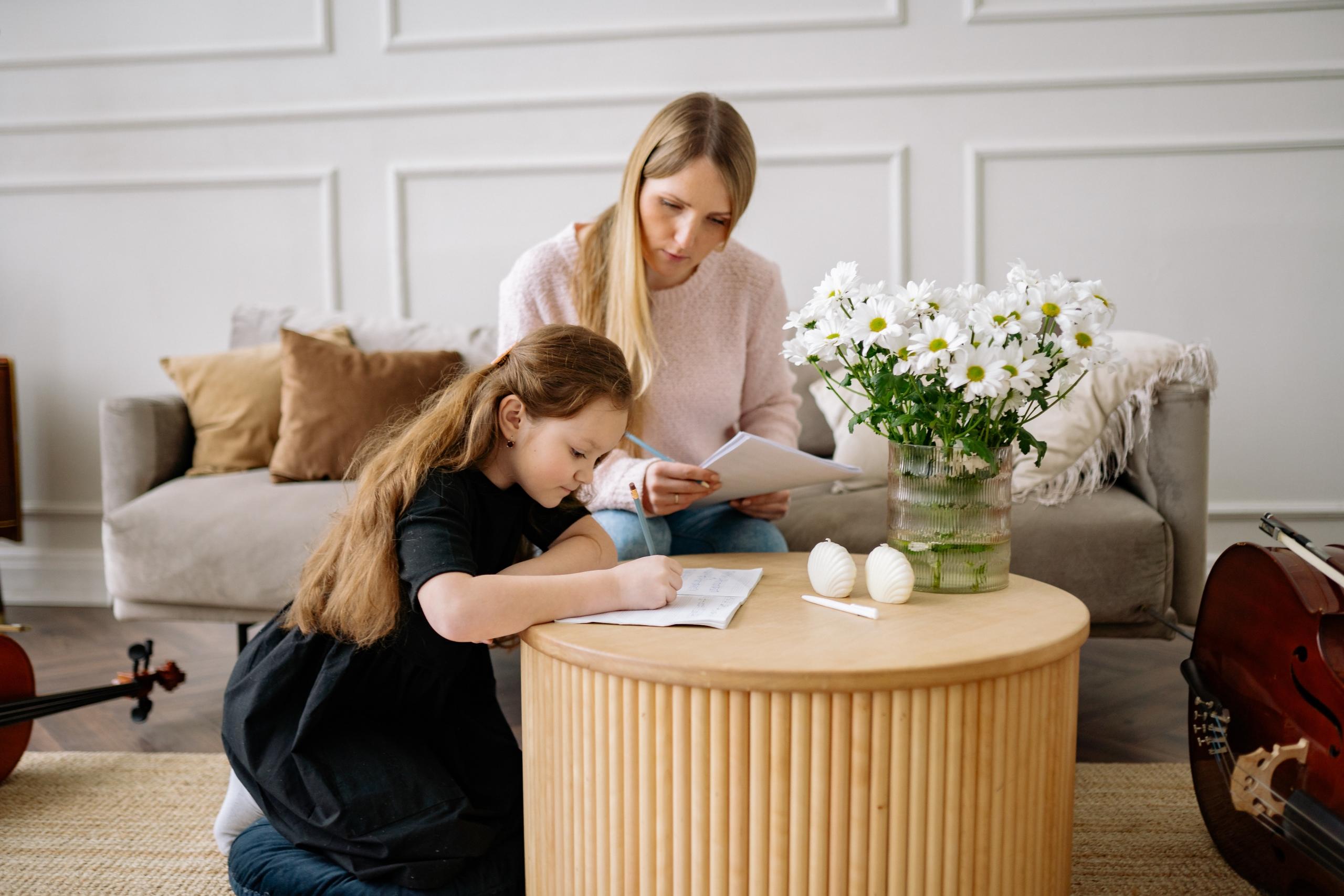 young girl working at coffee table as her private cello teacher watches over her