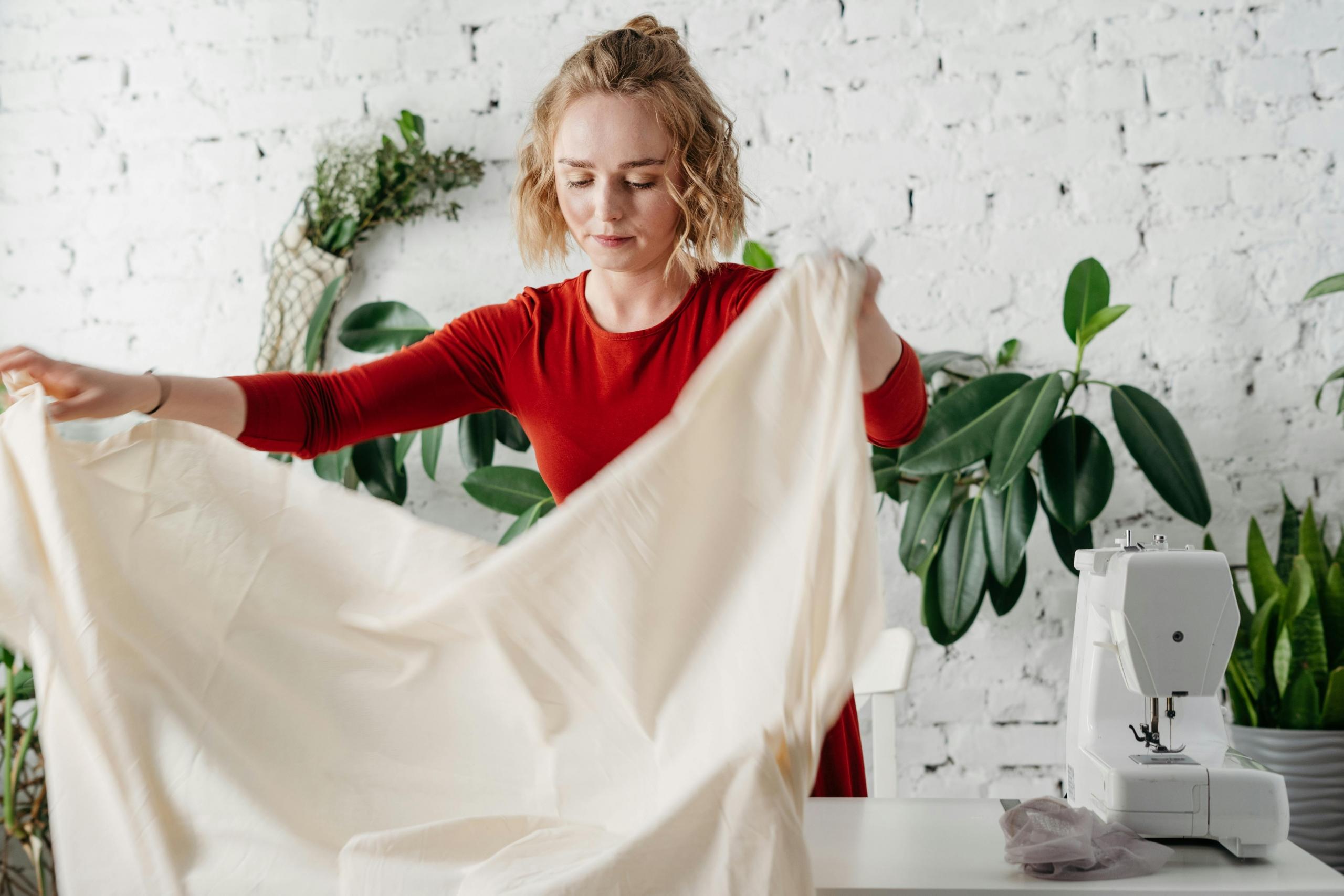 seamstress unrolling a bolt of cream fabric onto table with sewing machine