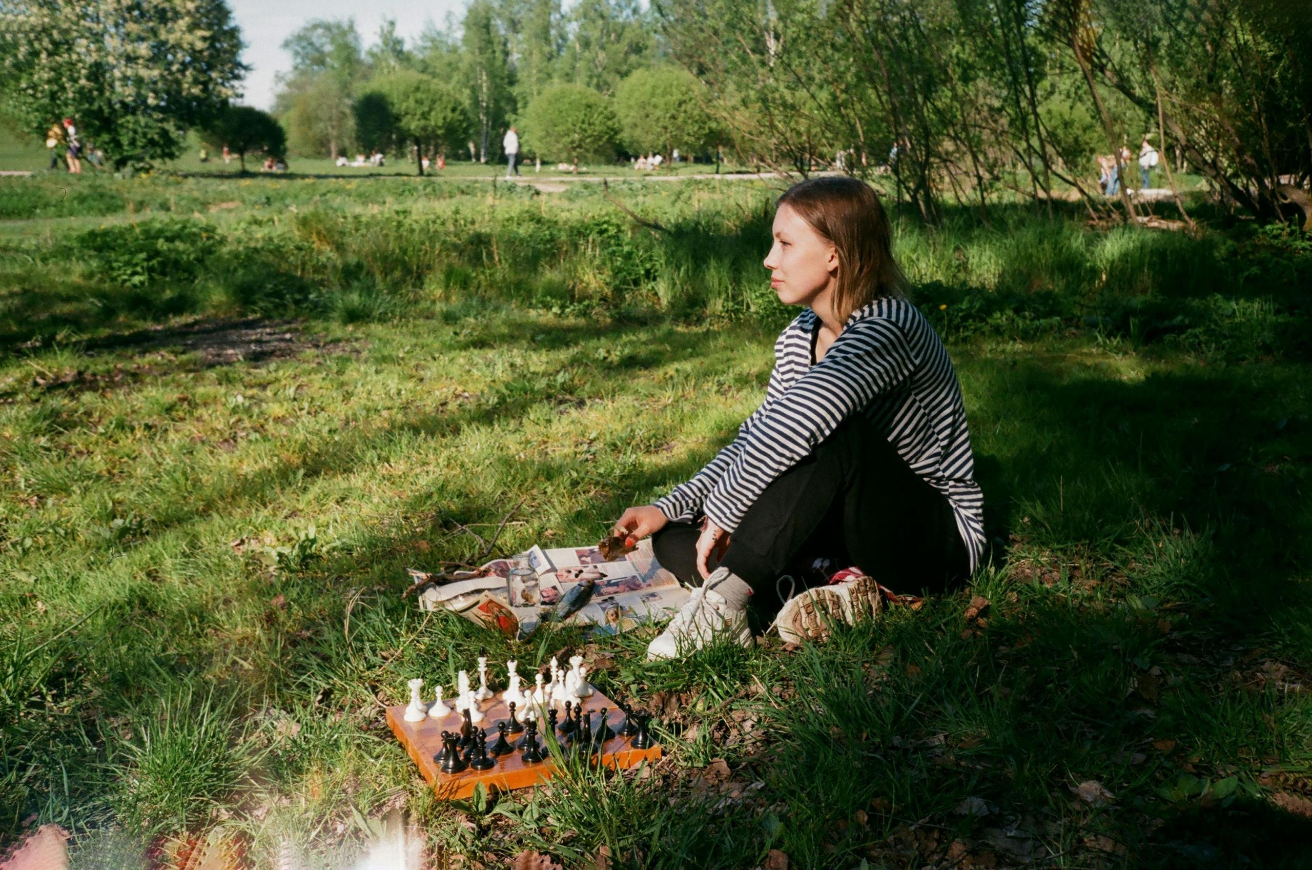 woman sitting in field of grass playing a solo game of chess