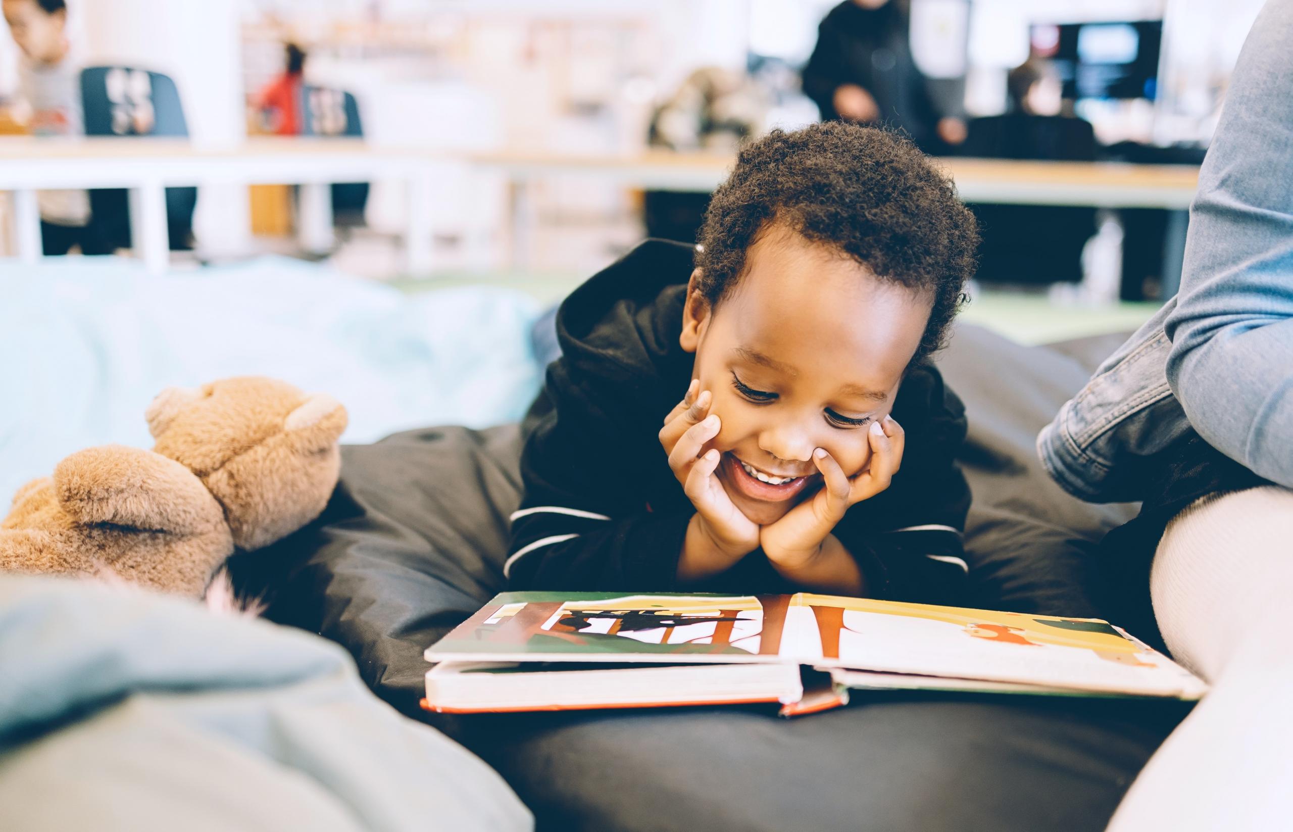 young boy lying on pouf in a library, reading a picture book