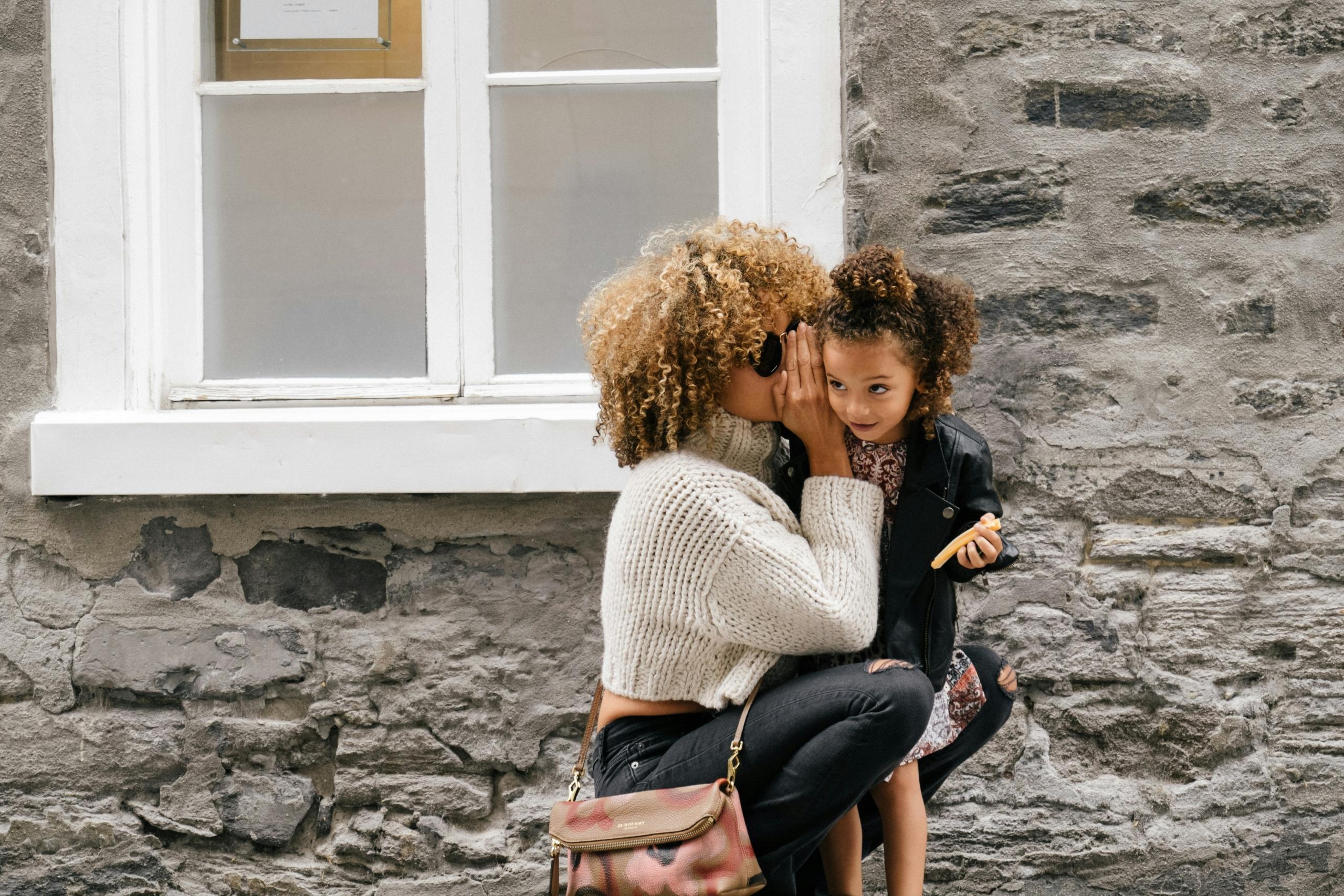 mom whispering in young daughter's ear