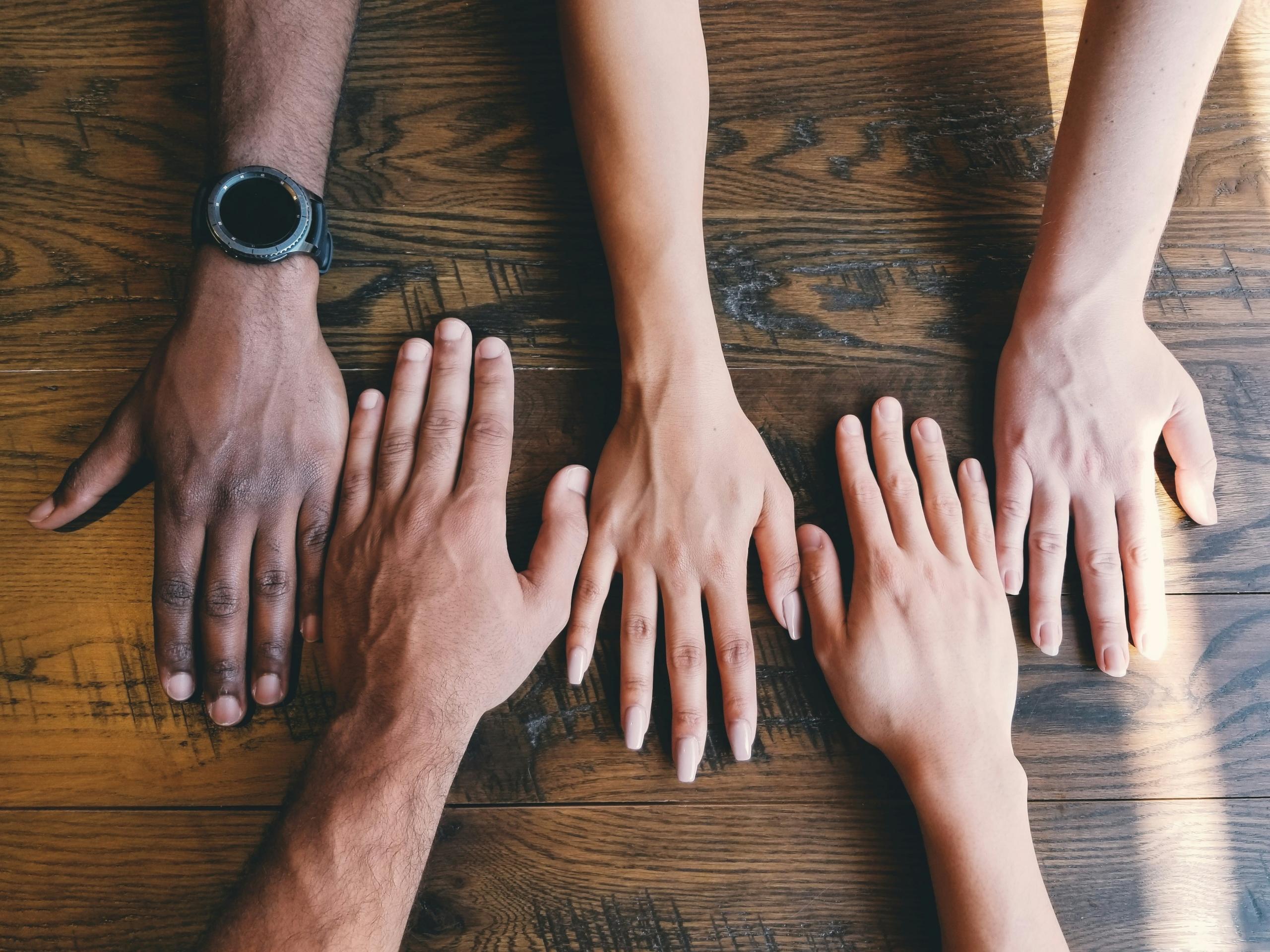 a group of people with their right hands placed on wooden tabletop