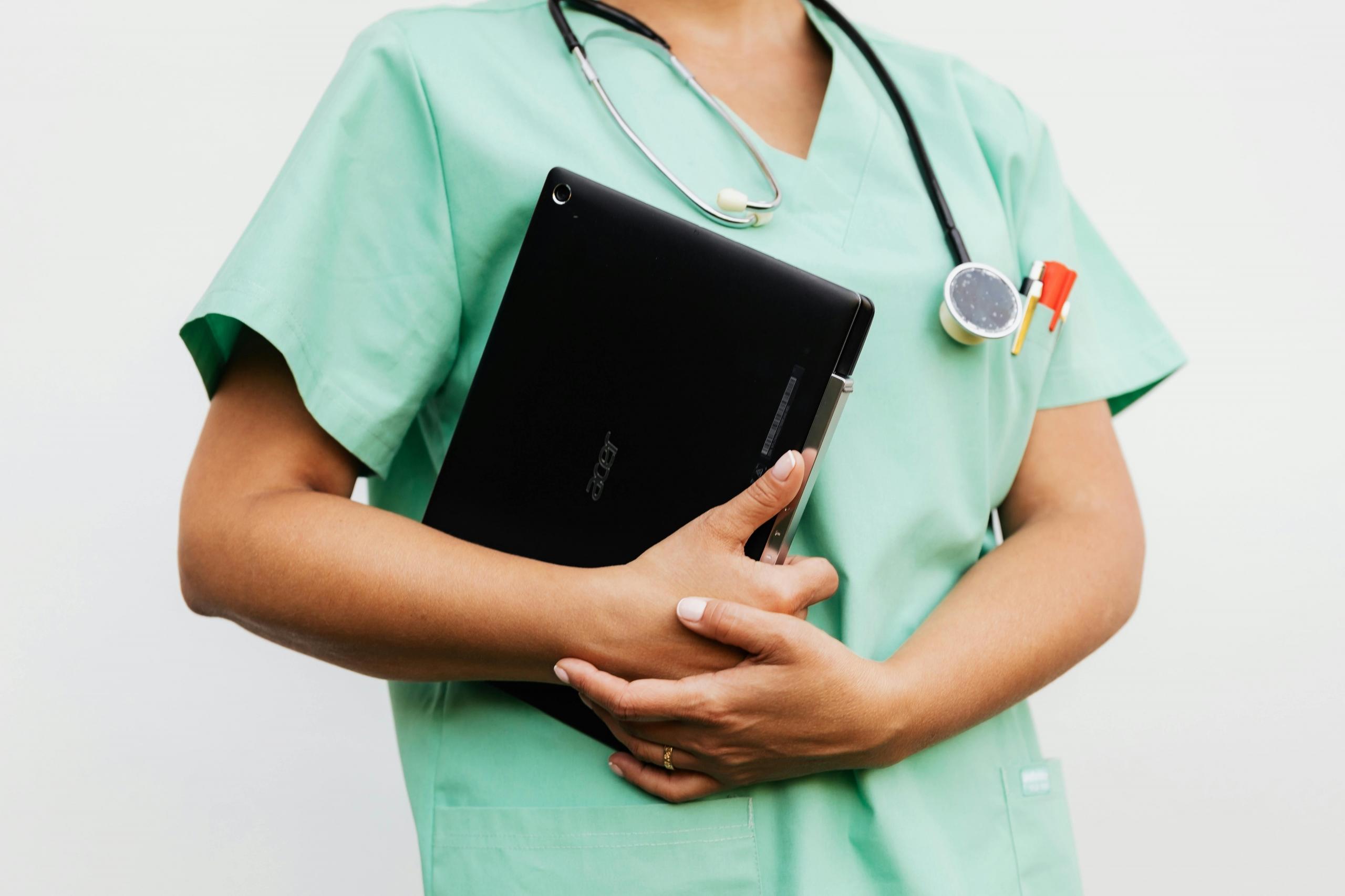 nurse in green scrubs holding ipad, with stethoscope around her neck
