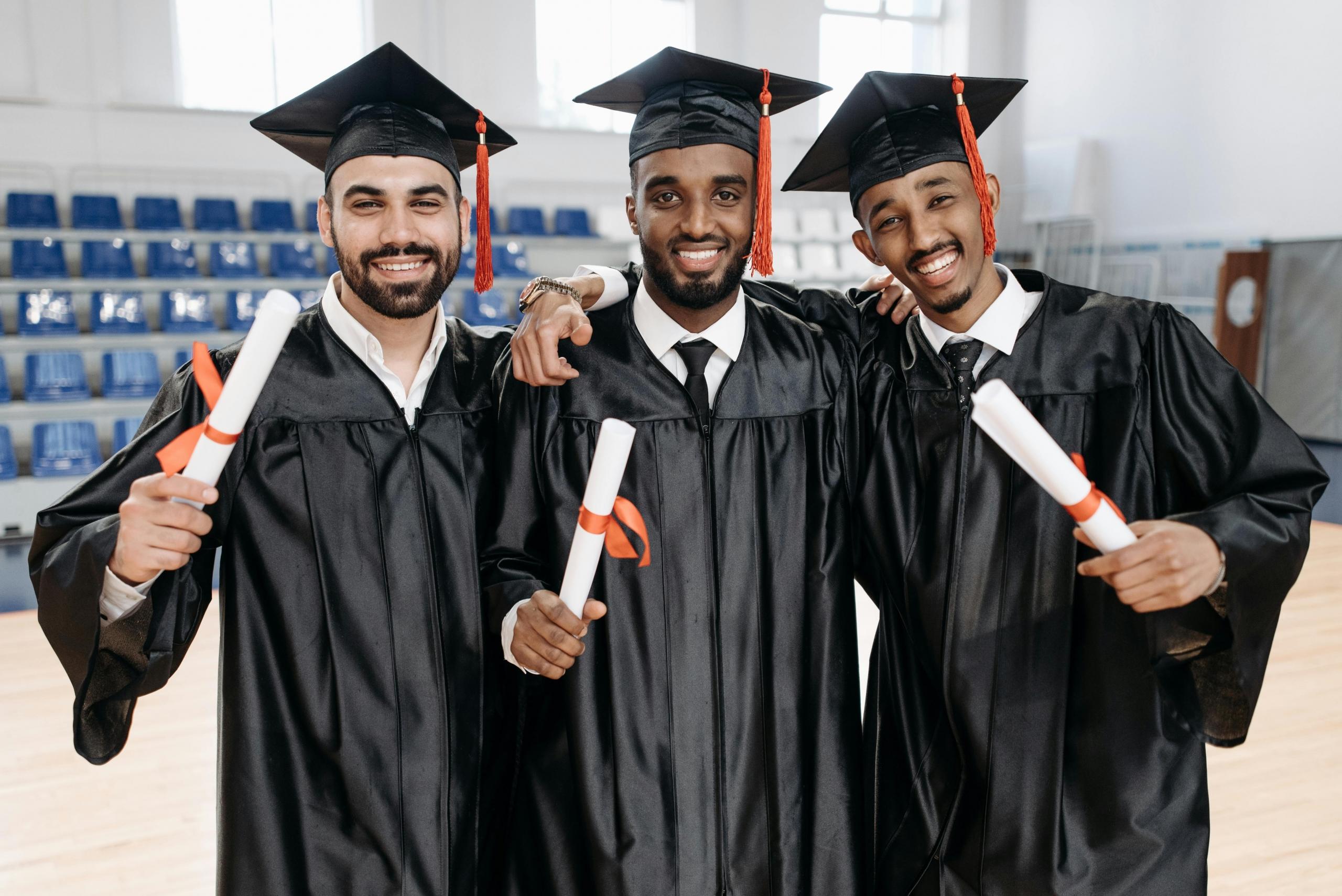 three students in graduation gowns and mortar boards holding diplomas