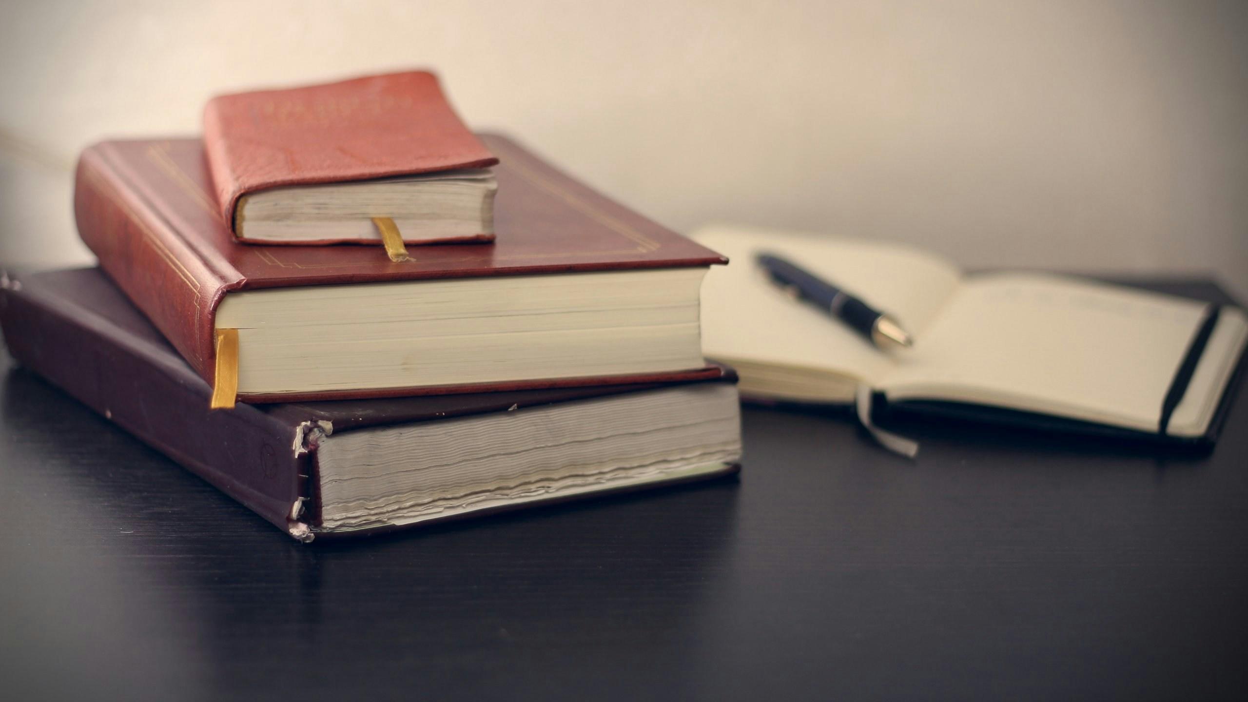 selective focus photography of three books beside opened notebook on table
