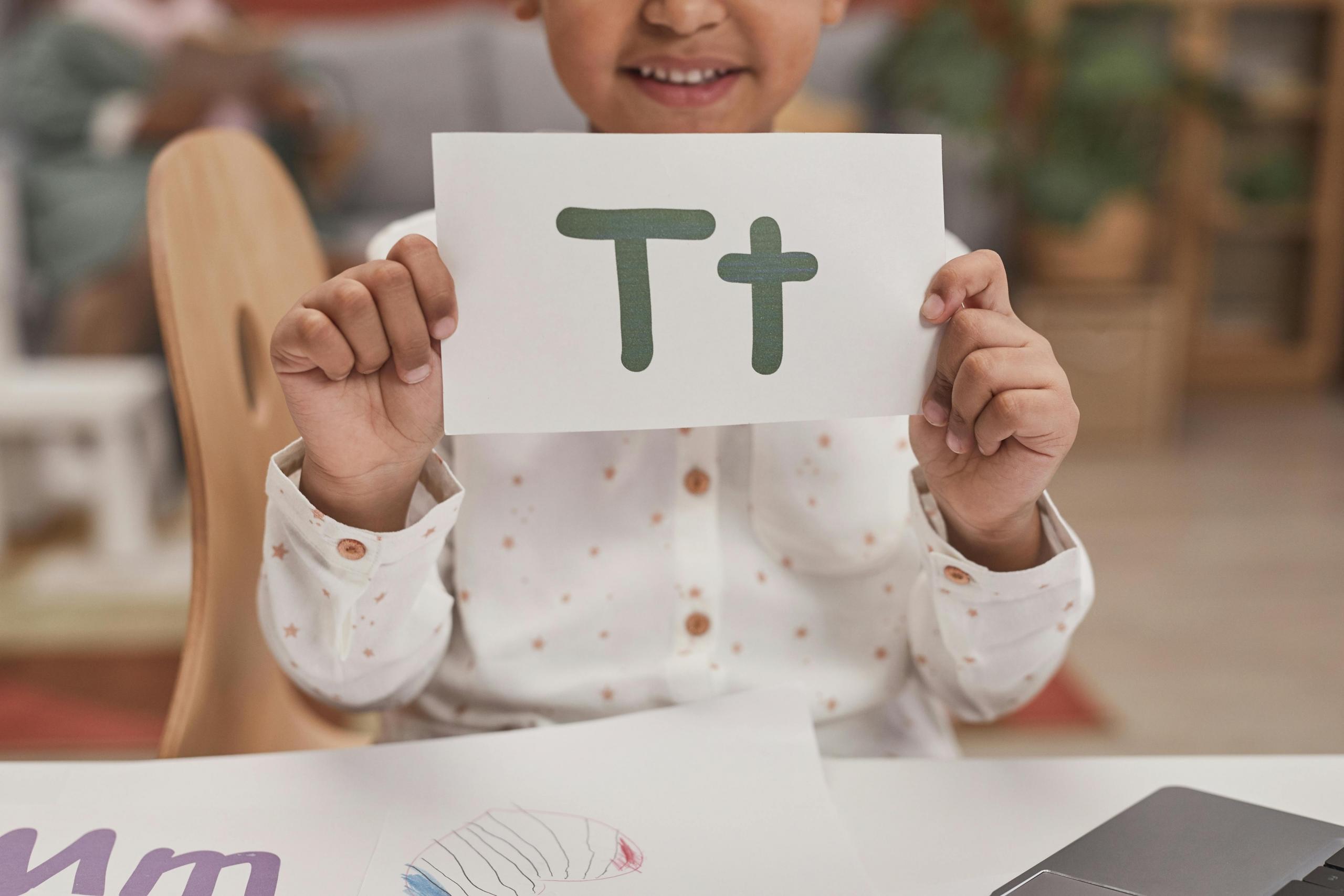 preschool girl holding up sign with the letter T written in capitals and lowercase