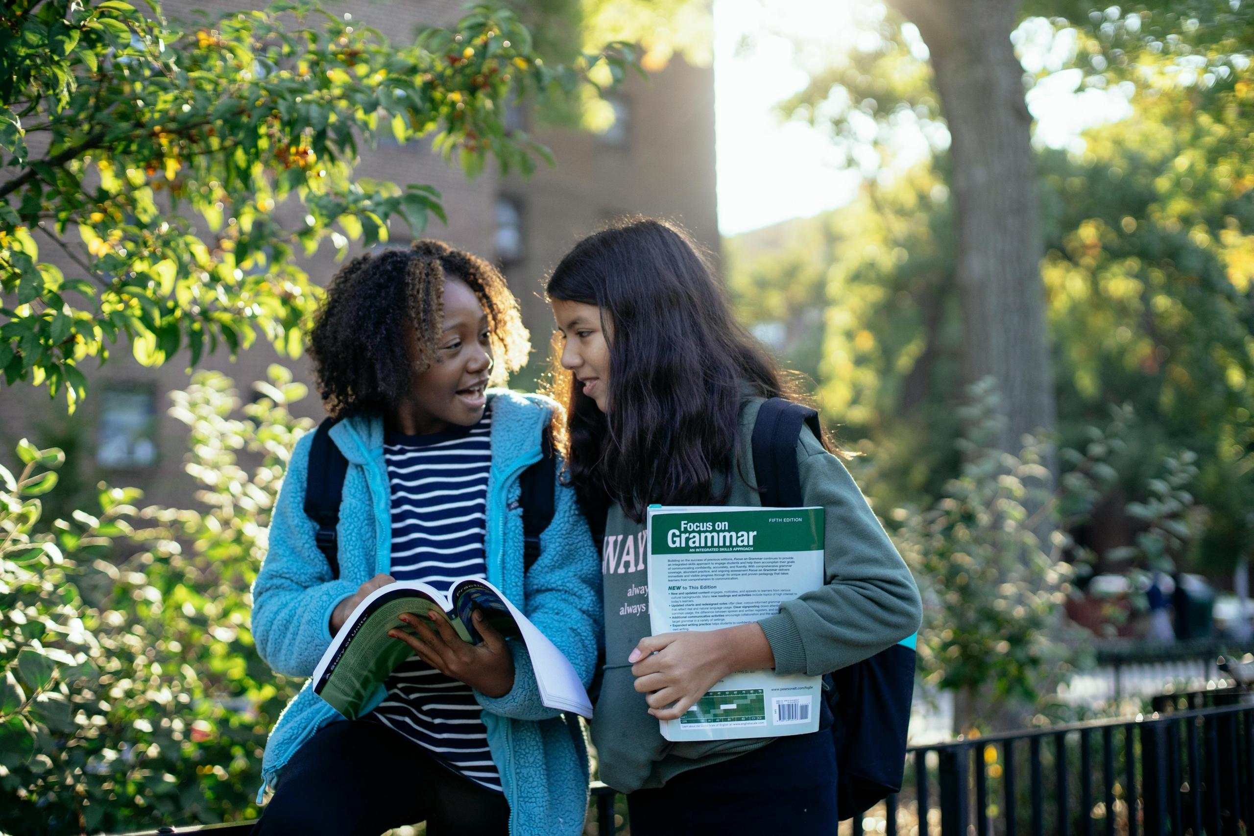 two schoolgirls walking outdoors carrying English textbooks
