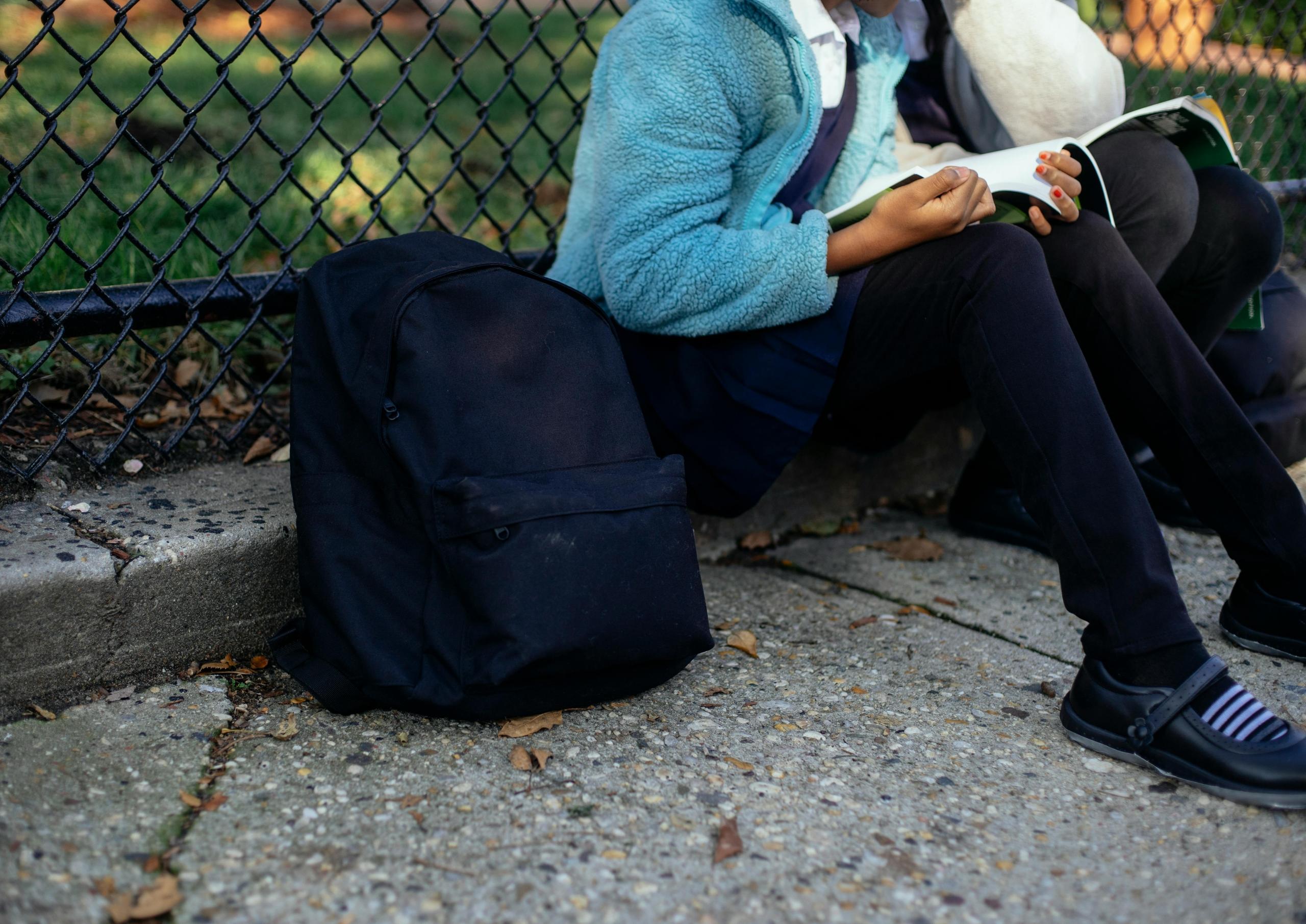 school girl sitting outside on the ground reading a workbook