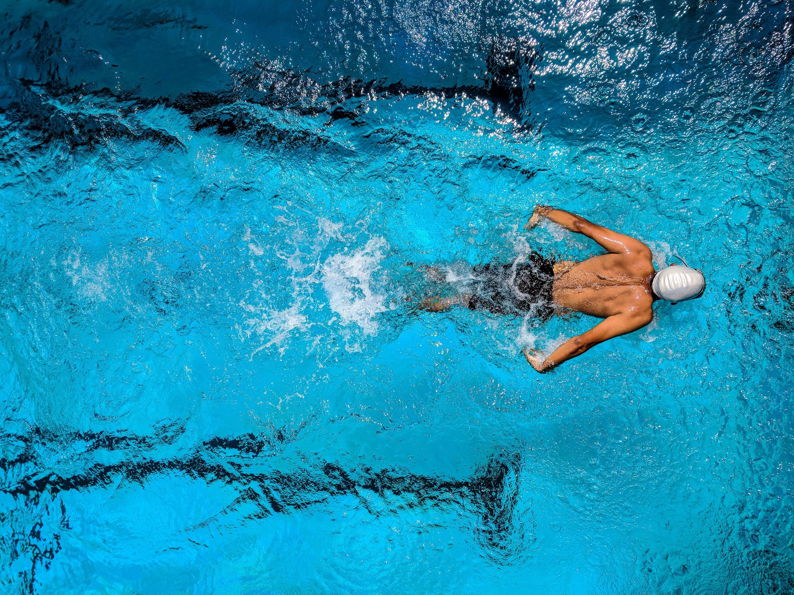 man swimming lengths in indoor pool wearing swimming cap