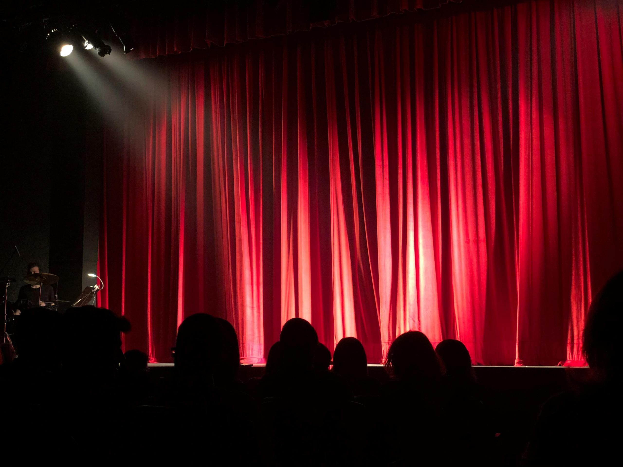 audience seated in a theatre with the stage curtain still closed