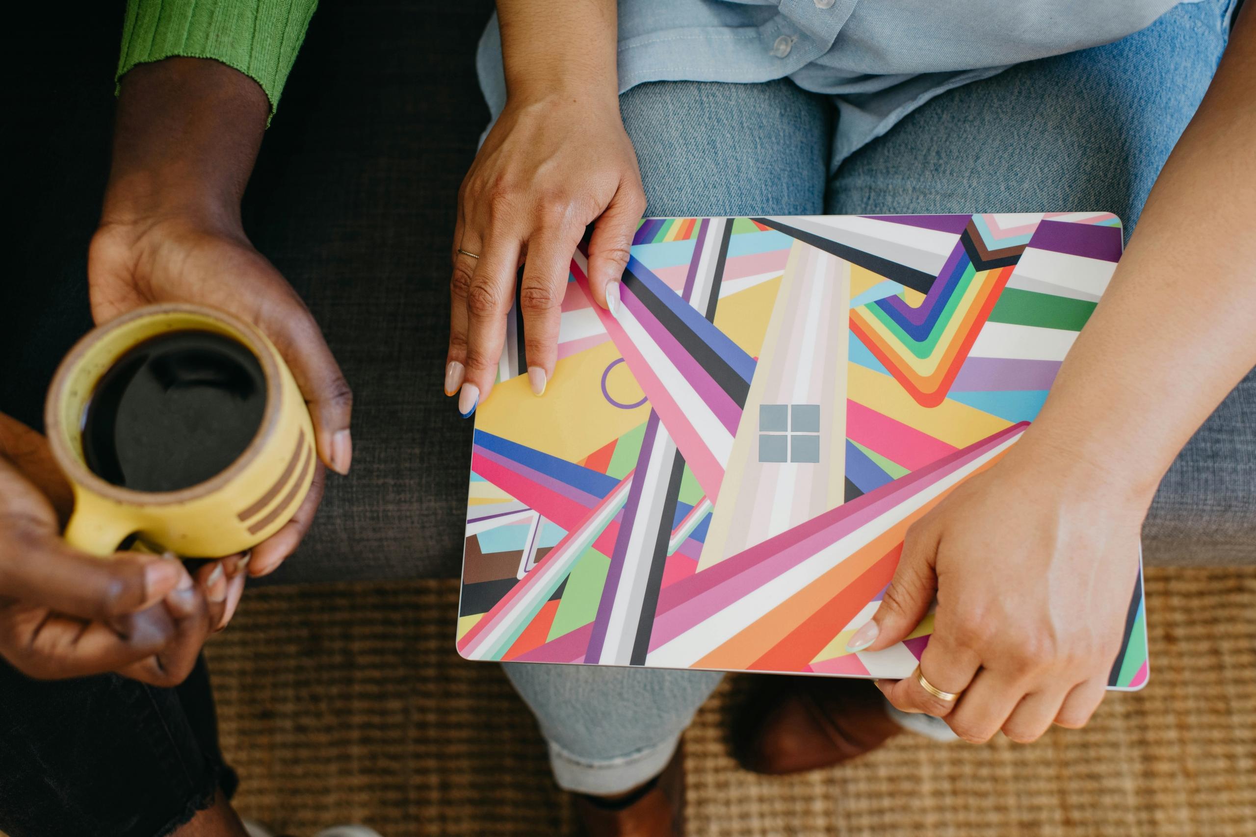close up of two people sitting on sofa holding a laptop and a cup of coffee