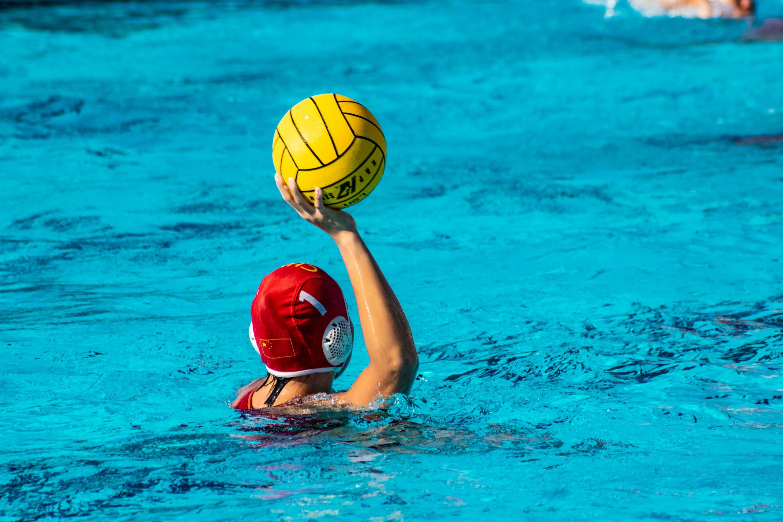 female water polo player holding yellow ball in the air