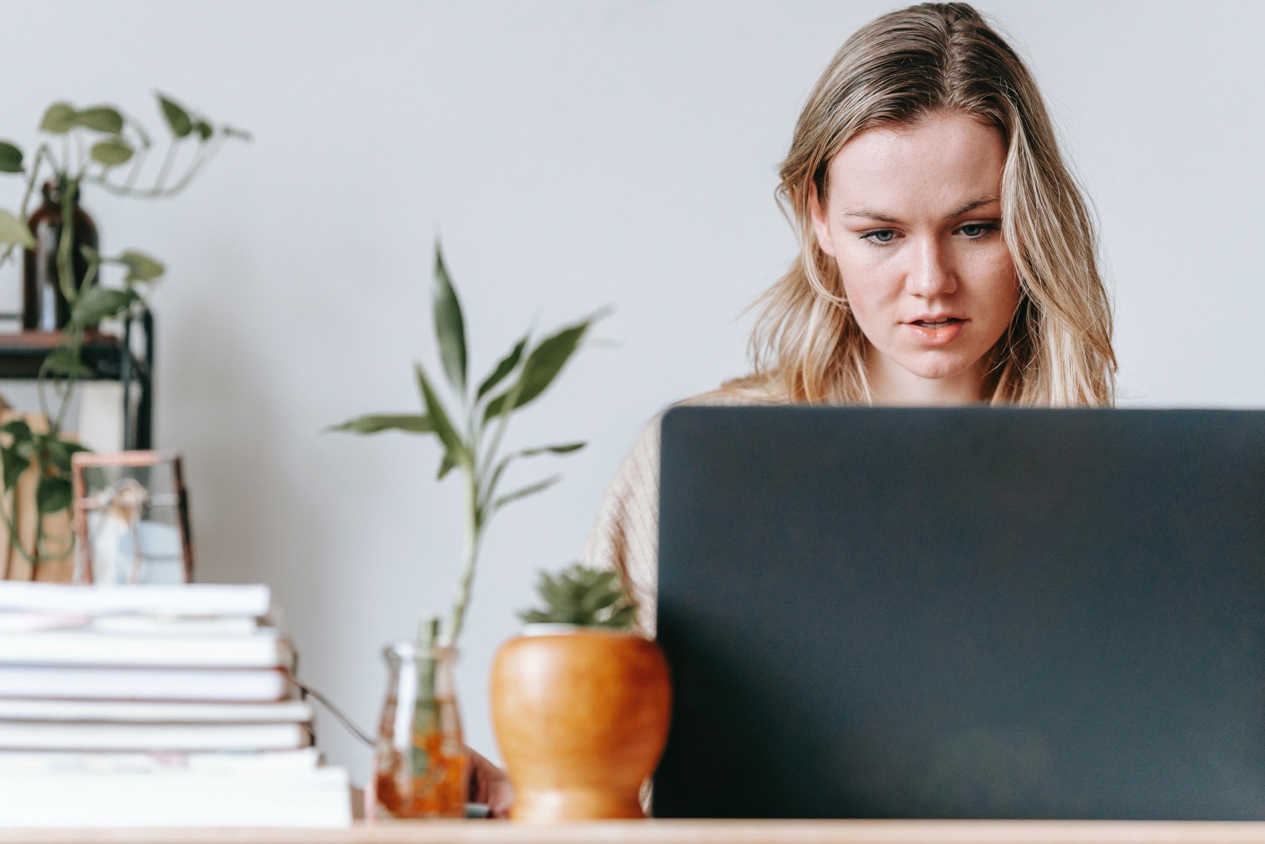 person sitting at desk working on computer with a pile of books alongside it