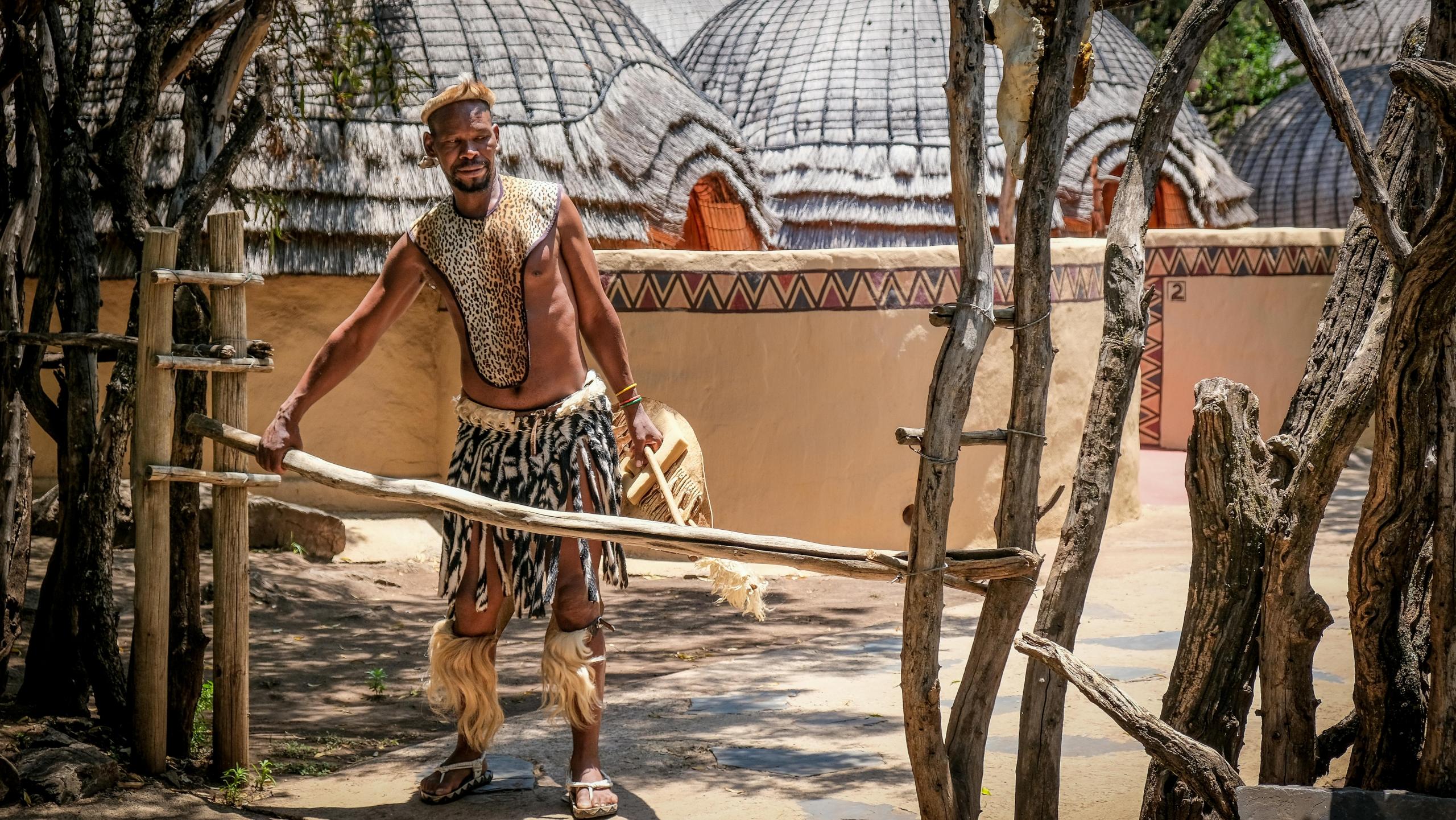 zulu man wearing traditional clothing and standing in front of traditional huts in village