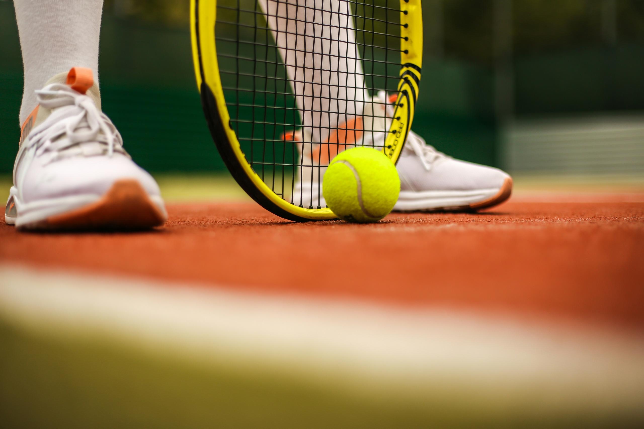 tennis ball on the ground in front of tennis racket held by tennis player