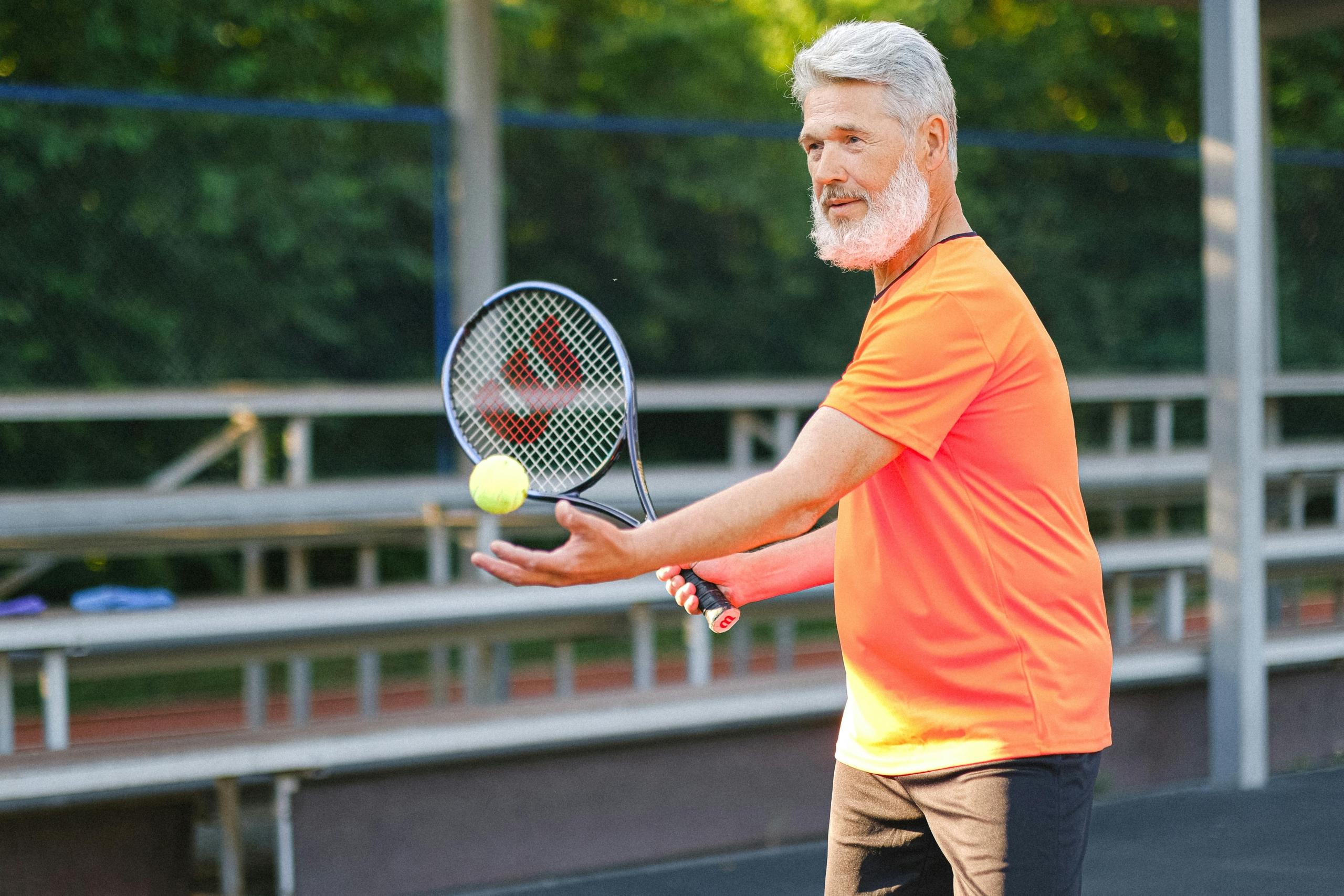 elderly person preparing the tennis ball for a serve