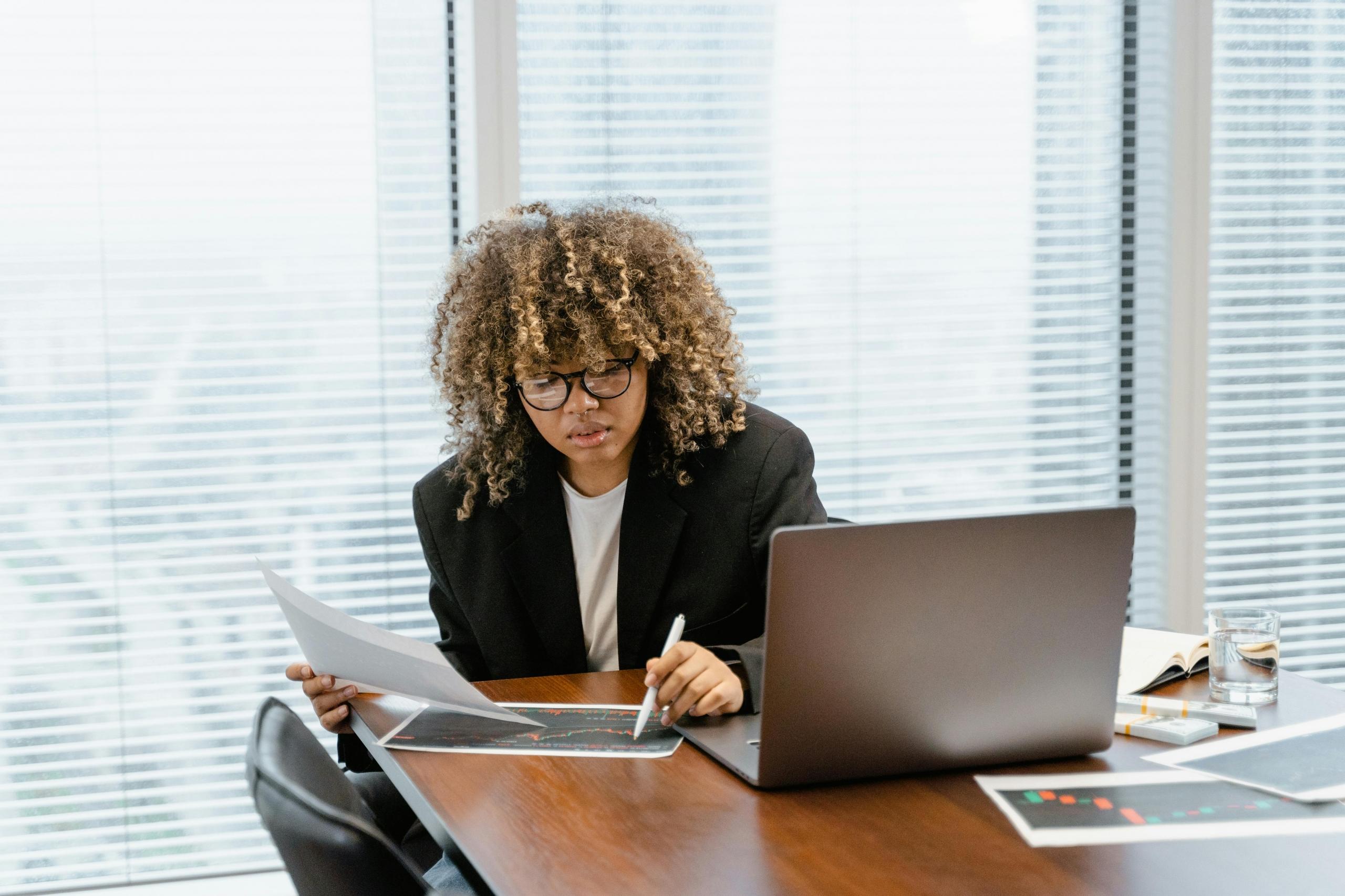 person sitting at desk in office building looking at graphs and data on paper and on computer