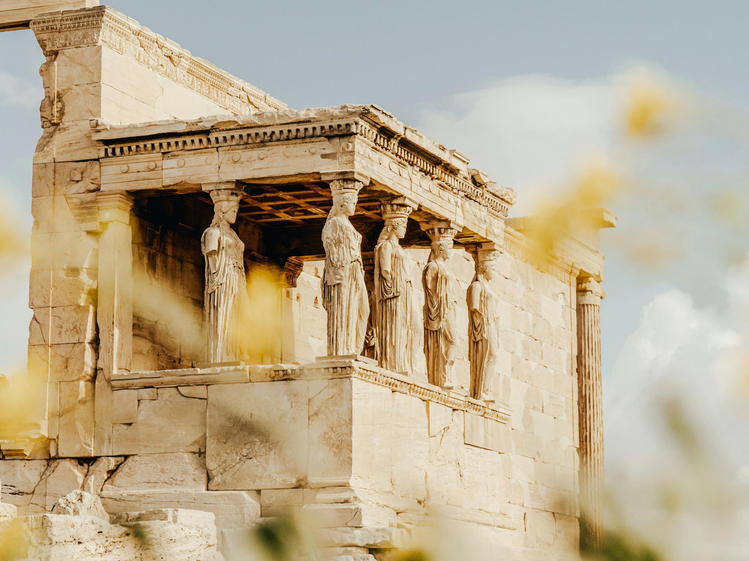 greek temple with statues seen through nearby vegetation