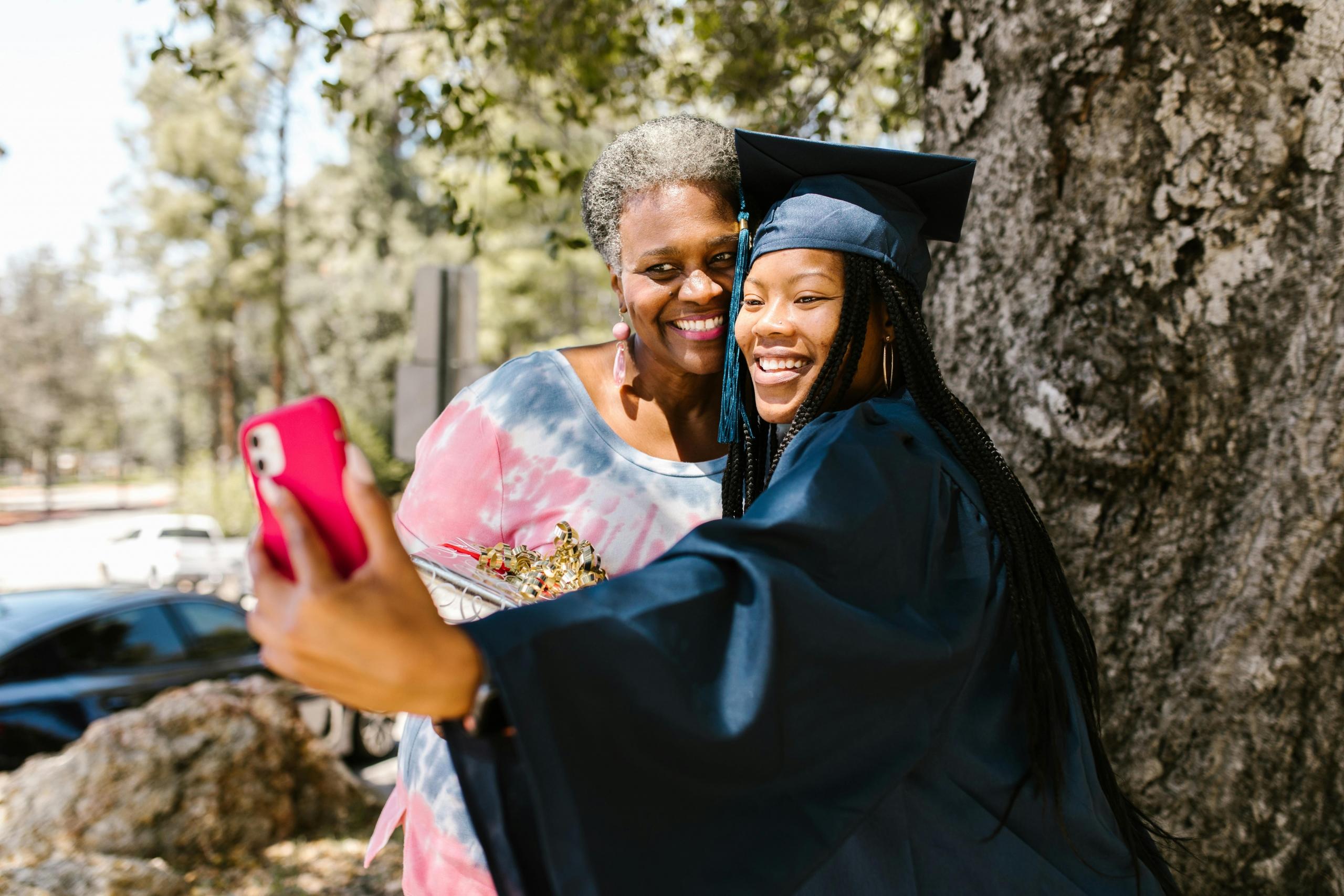 student graduating wearing graduation gown and mortar board taking a selfie with her mom