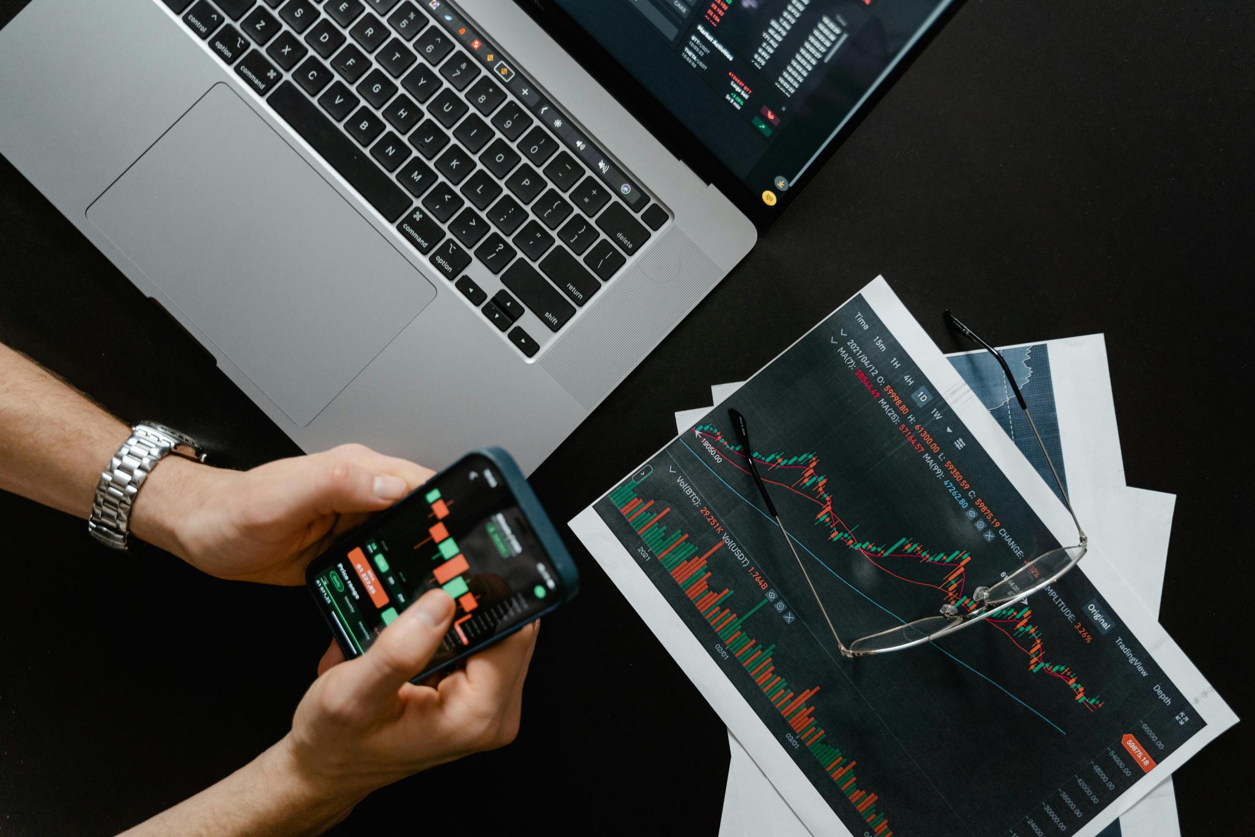 person looking at graphs and data on paper, smartphone and on computer