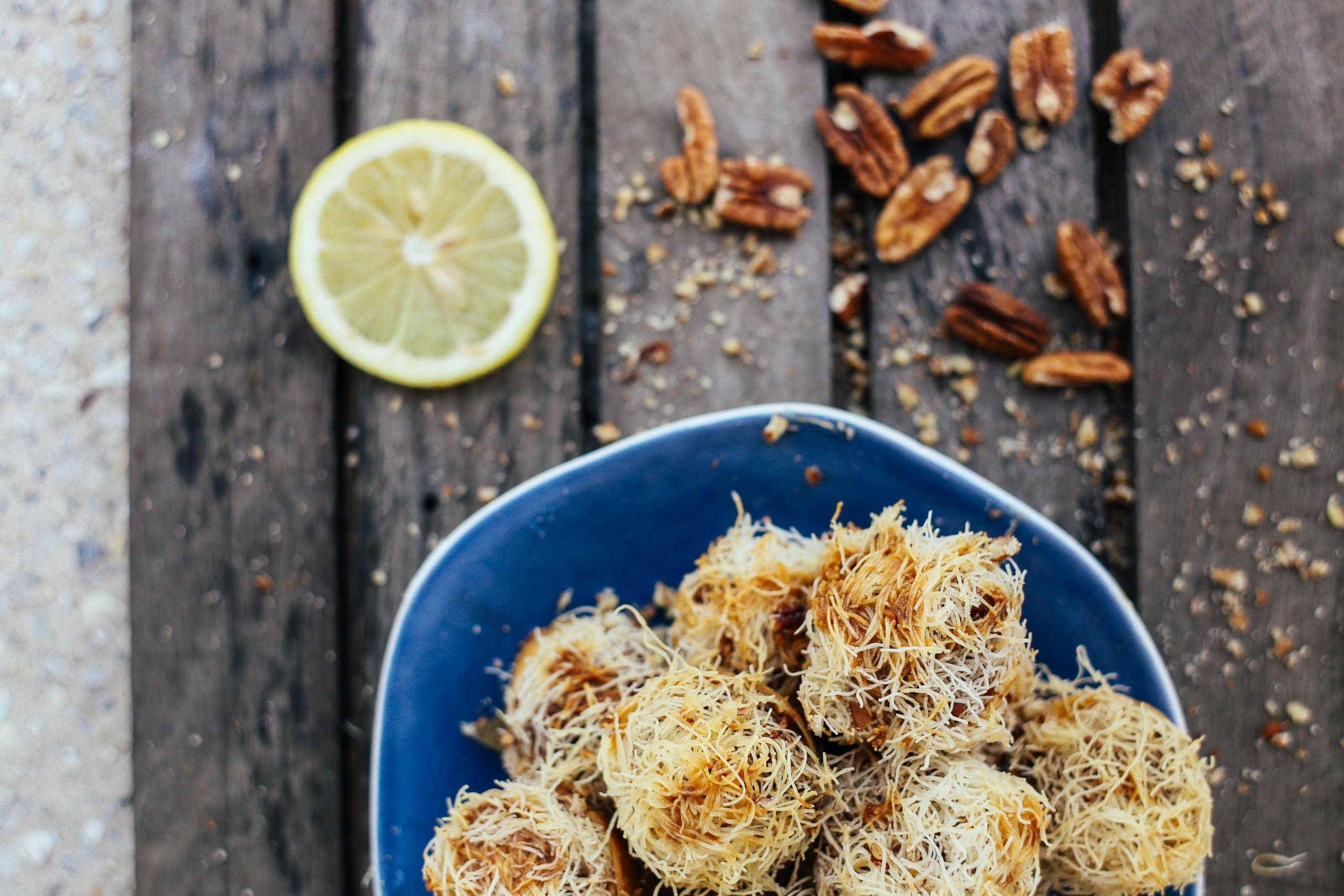a bowl of Kataifi next to pecan nuts and a slice of lemon