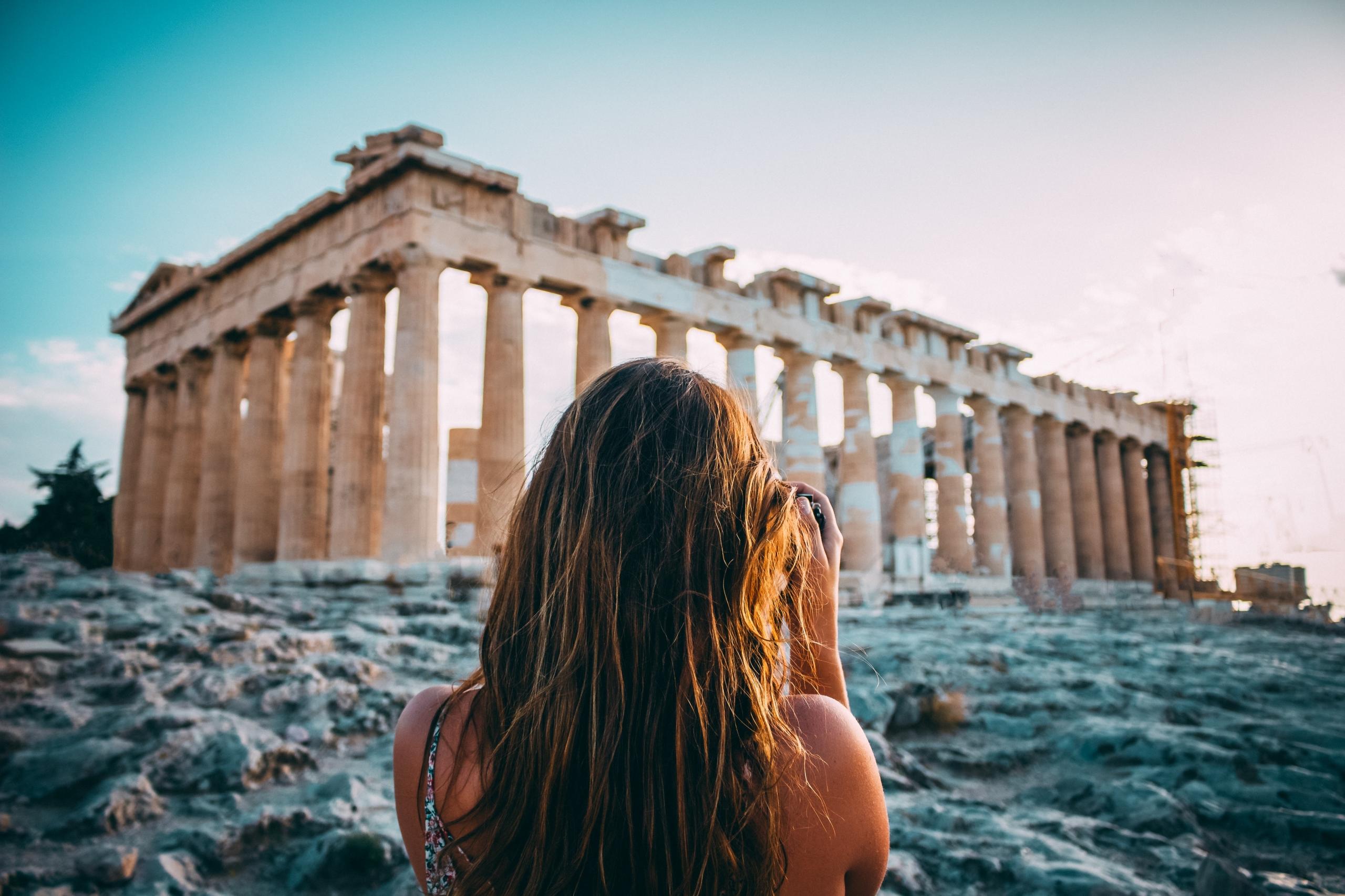 woman facing the acropolis in athens greece taking a photo at dusk