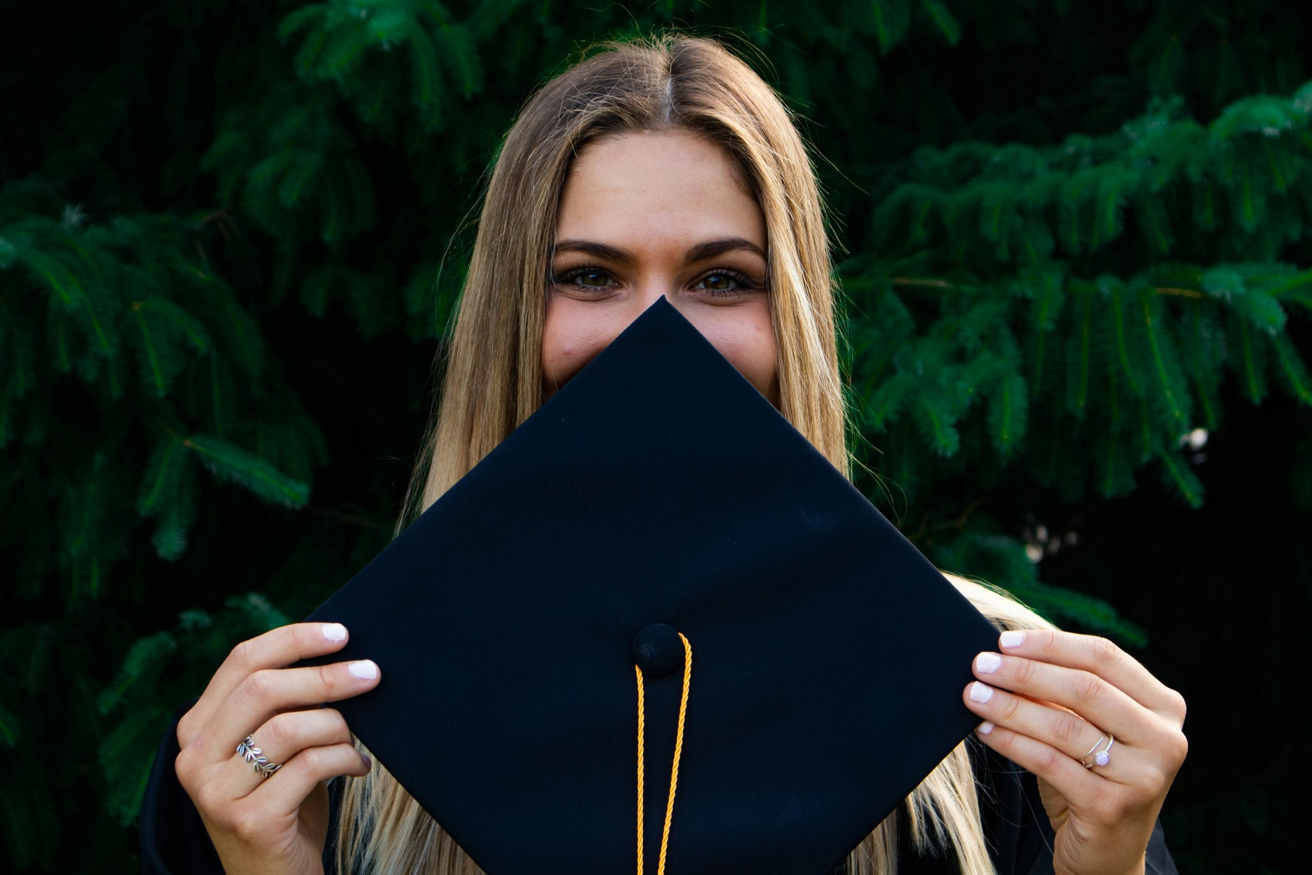 graduating student holding black mortar board up to face
