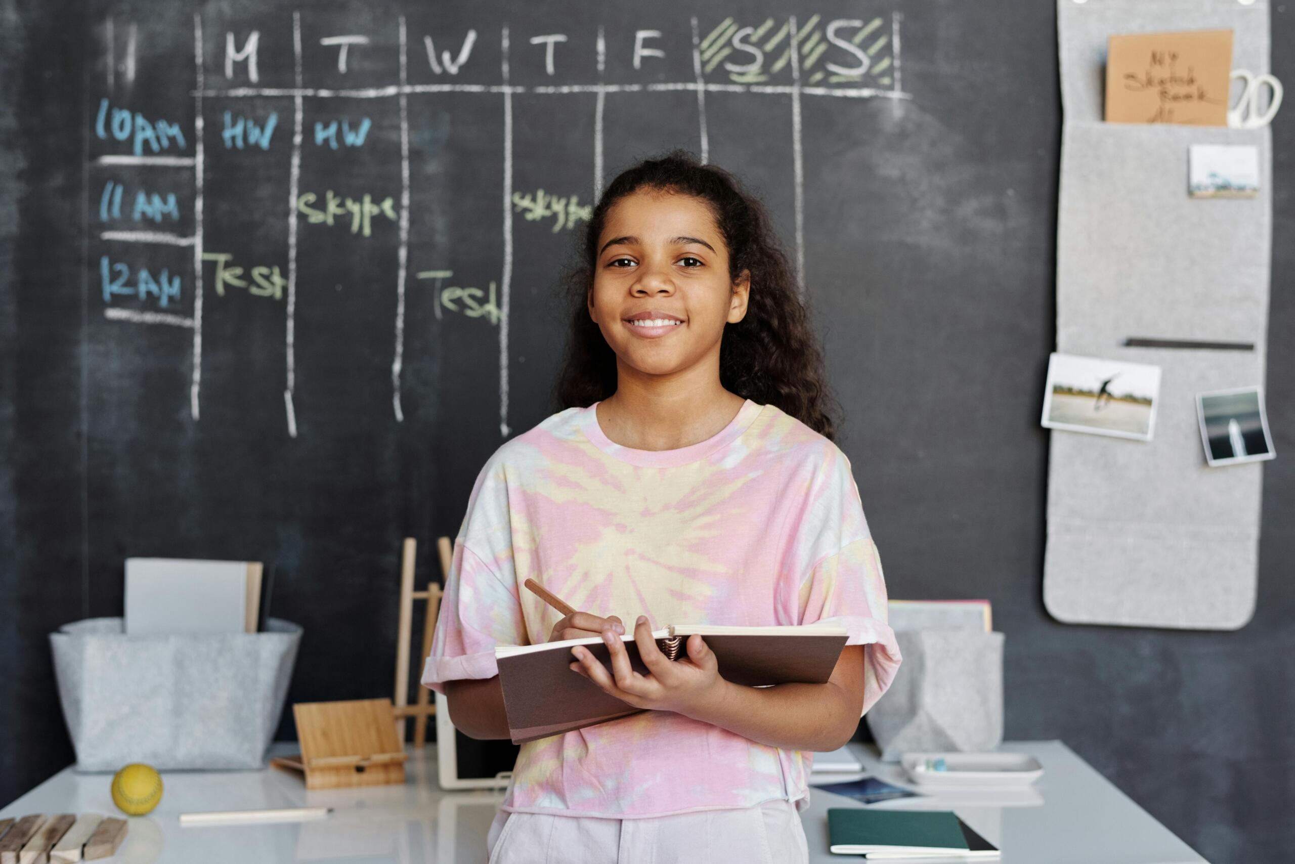 smiling student standing in front of a blackboard with a weekly planner written in chalk
