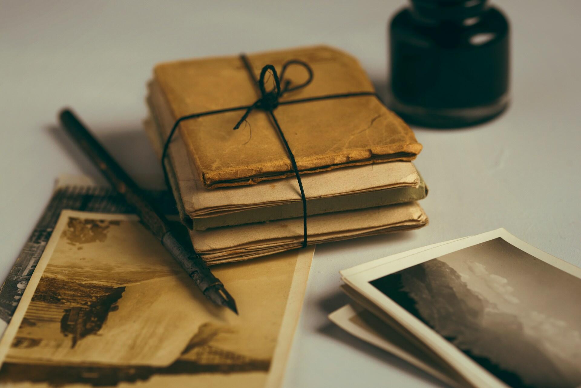 discoloured antique  books bound together with string on a table next to old photographs