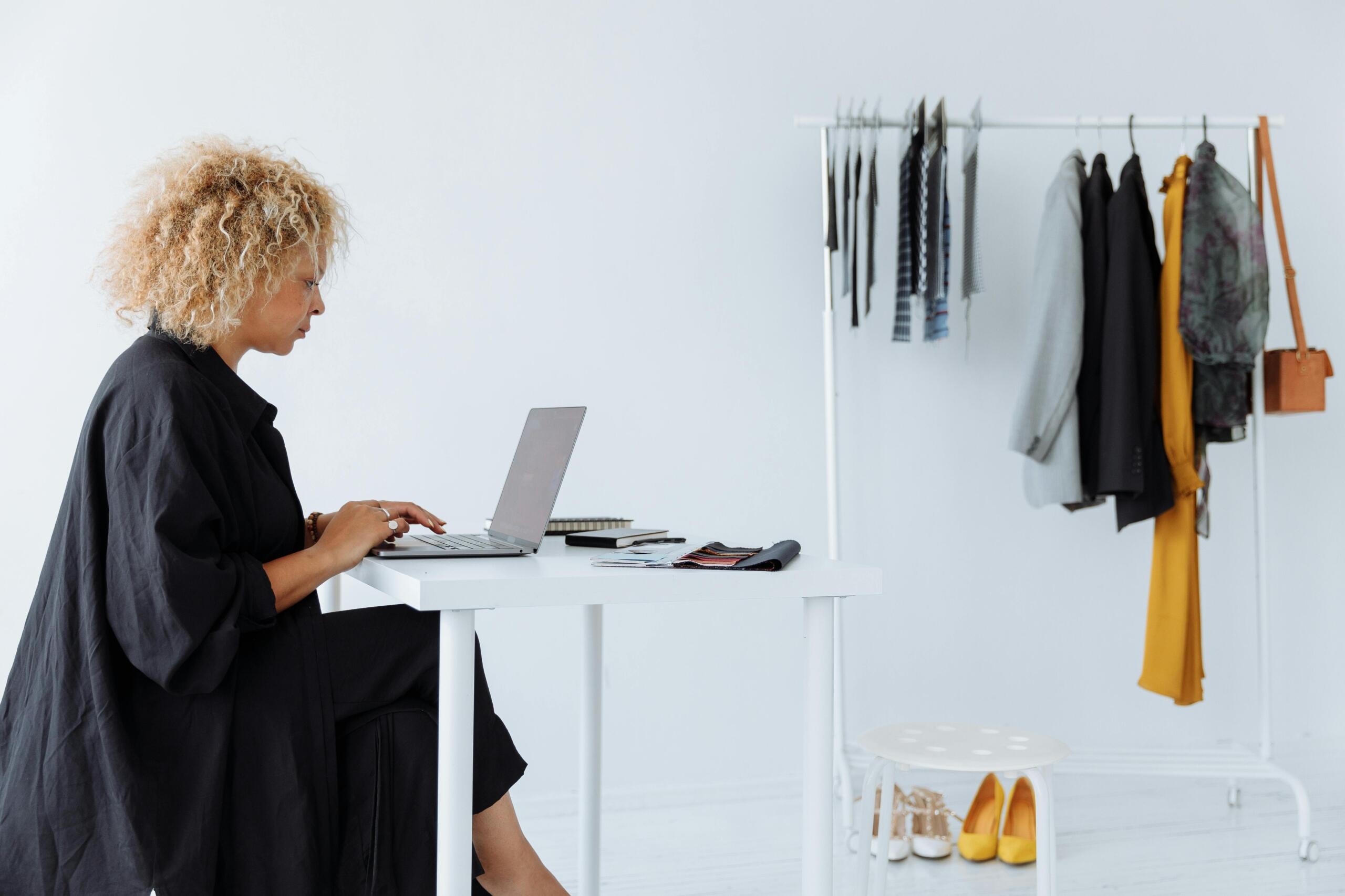 woman sitting at desk in white room with rail of clothing against a wall