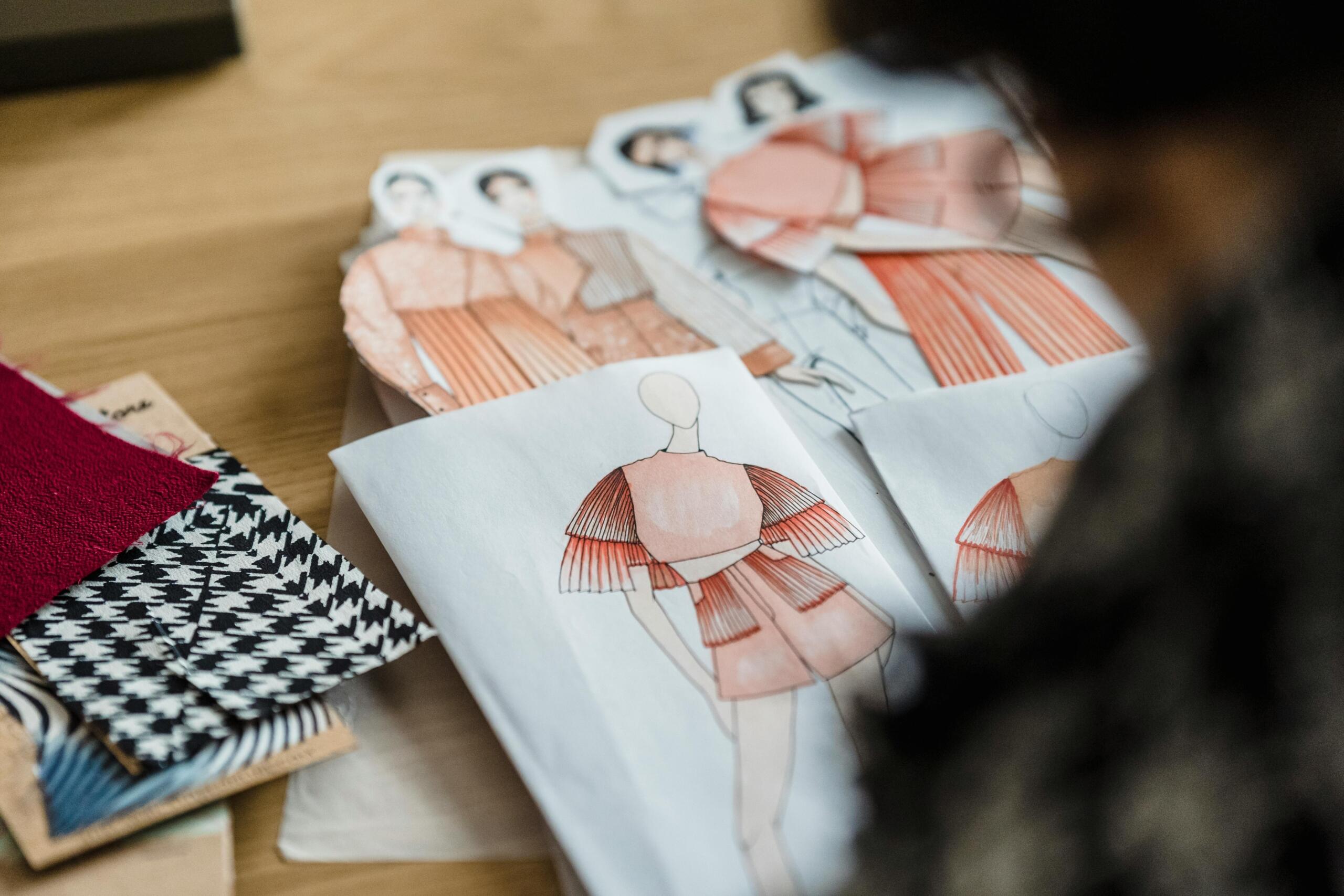 over the shoulder photo of designer working at table with fabric samples and clothing illustrations