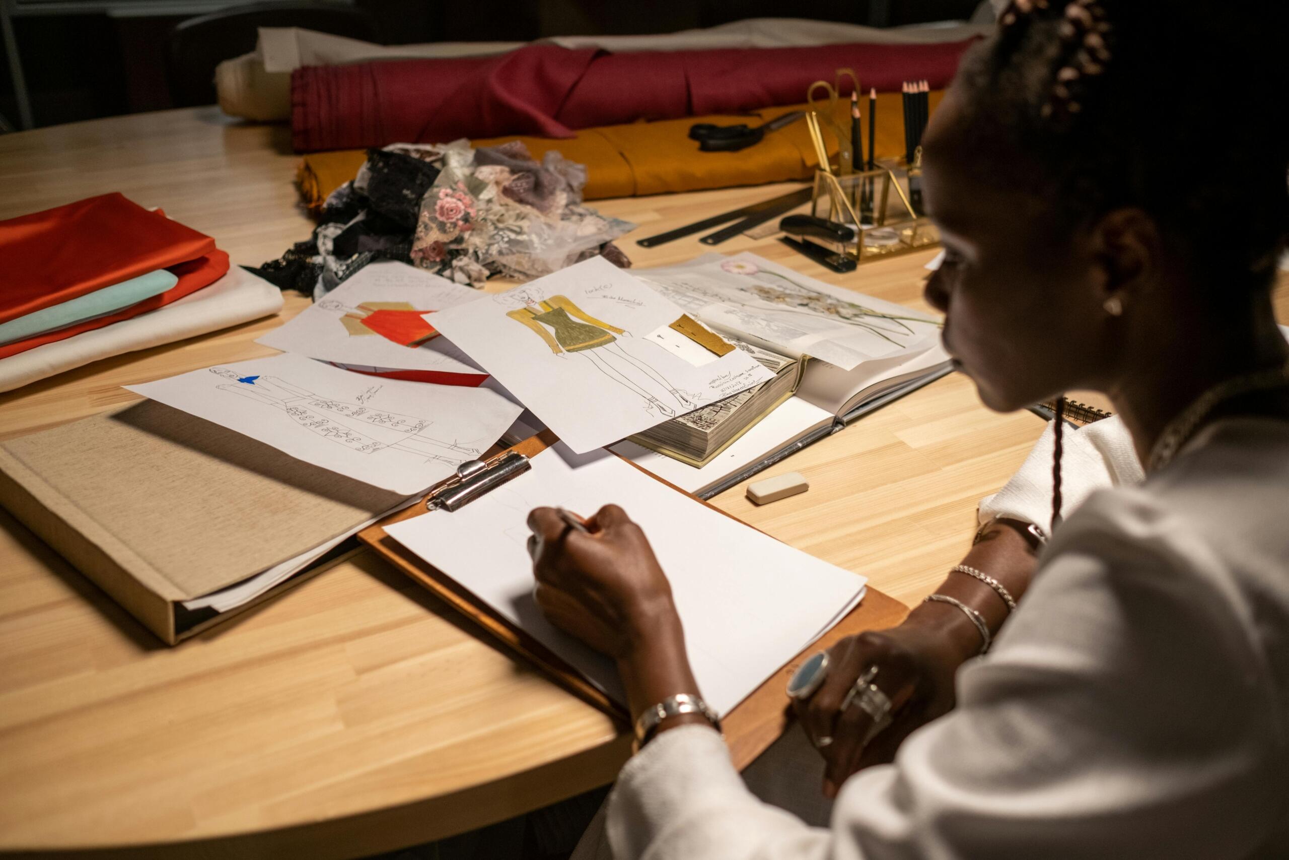 woman seated behind desk creating fashion designs on paper