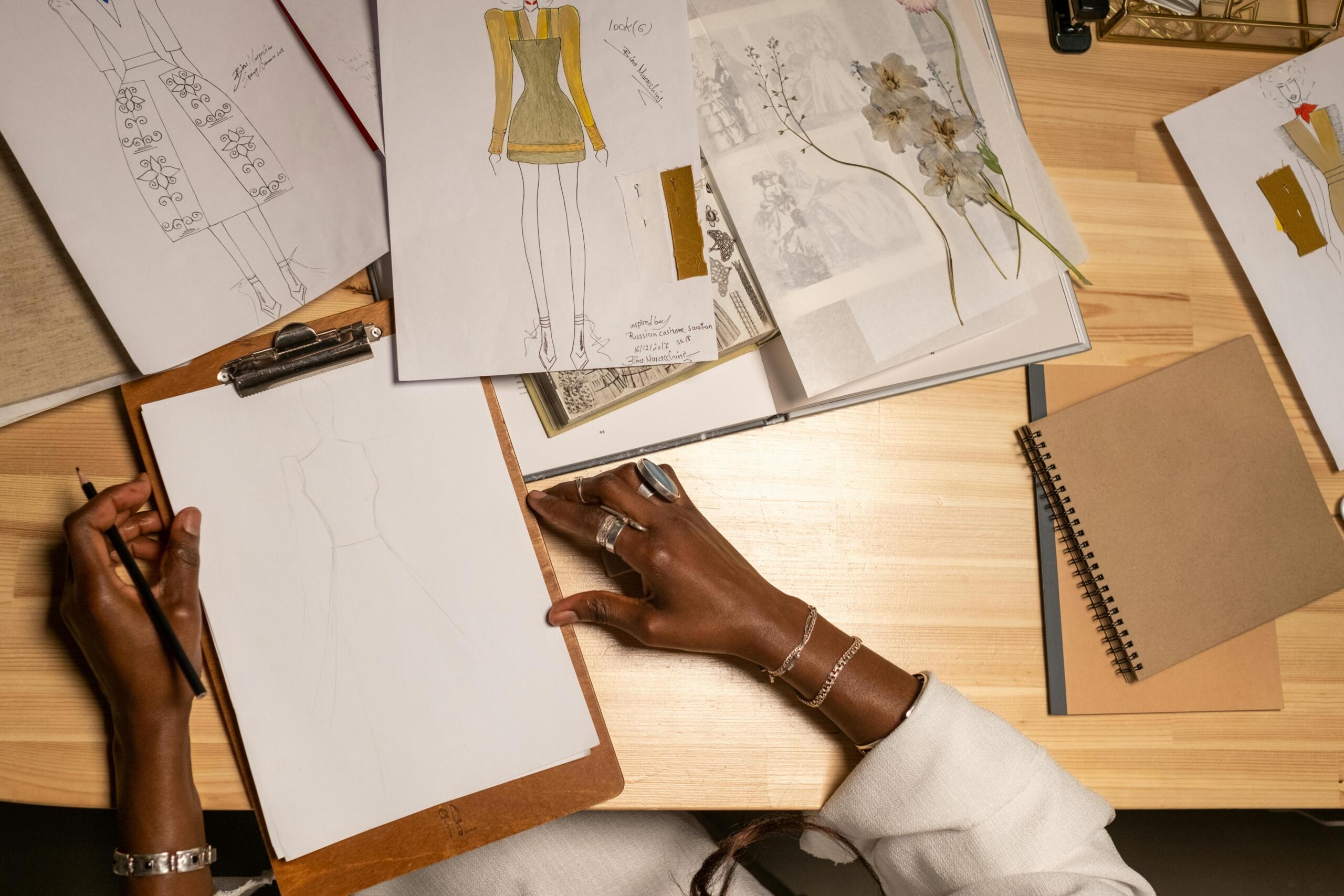 fashion designer seated behind desk creating fashion designs on paper