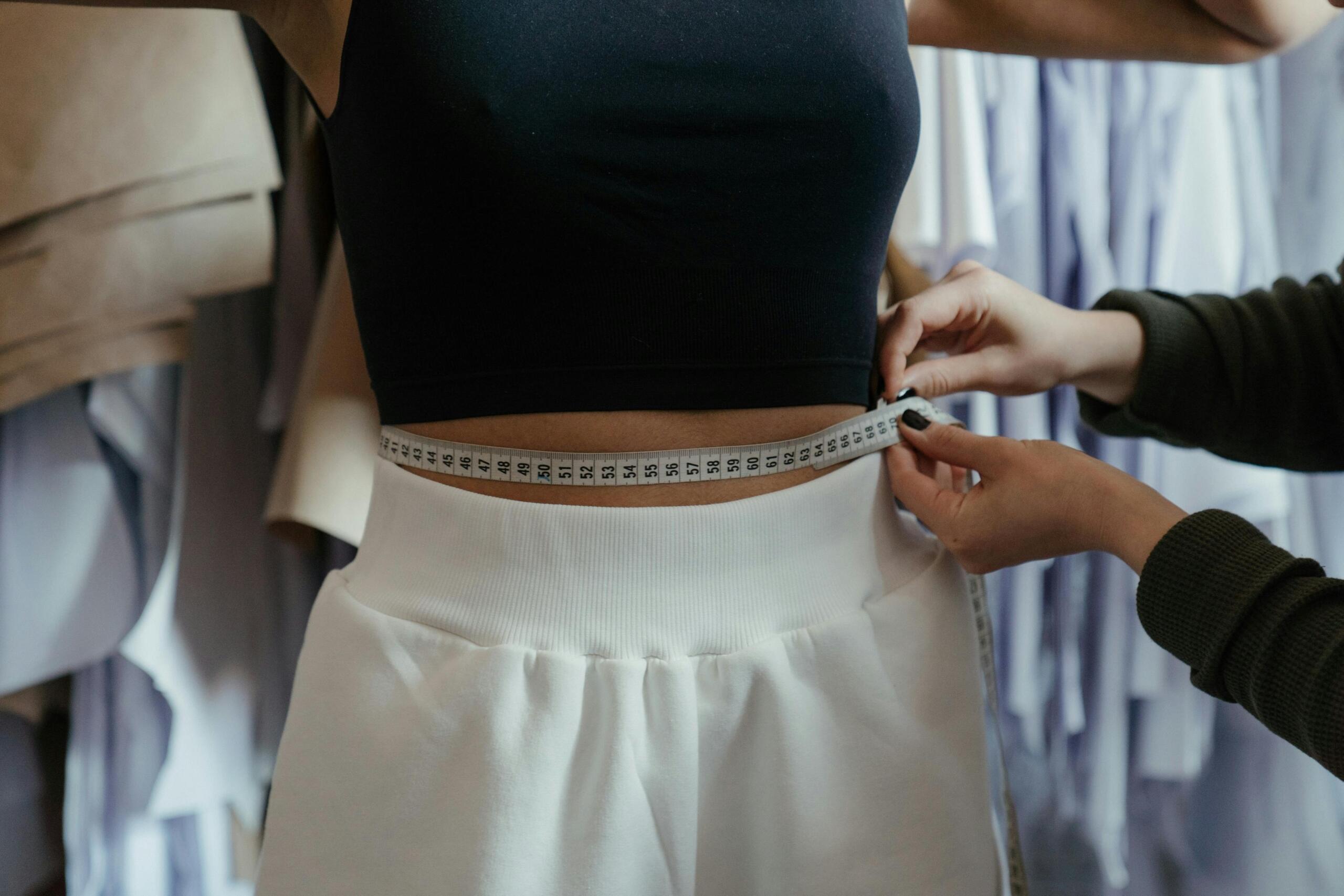 fashion designer using tape measure to measure the waist of a model