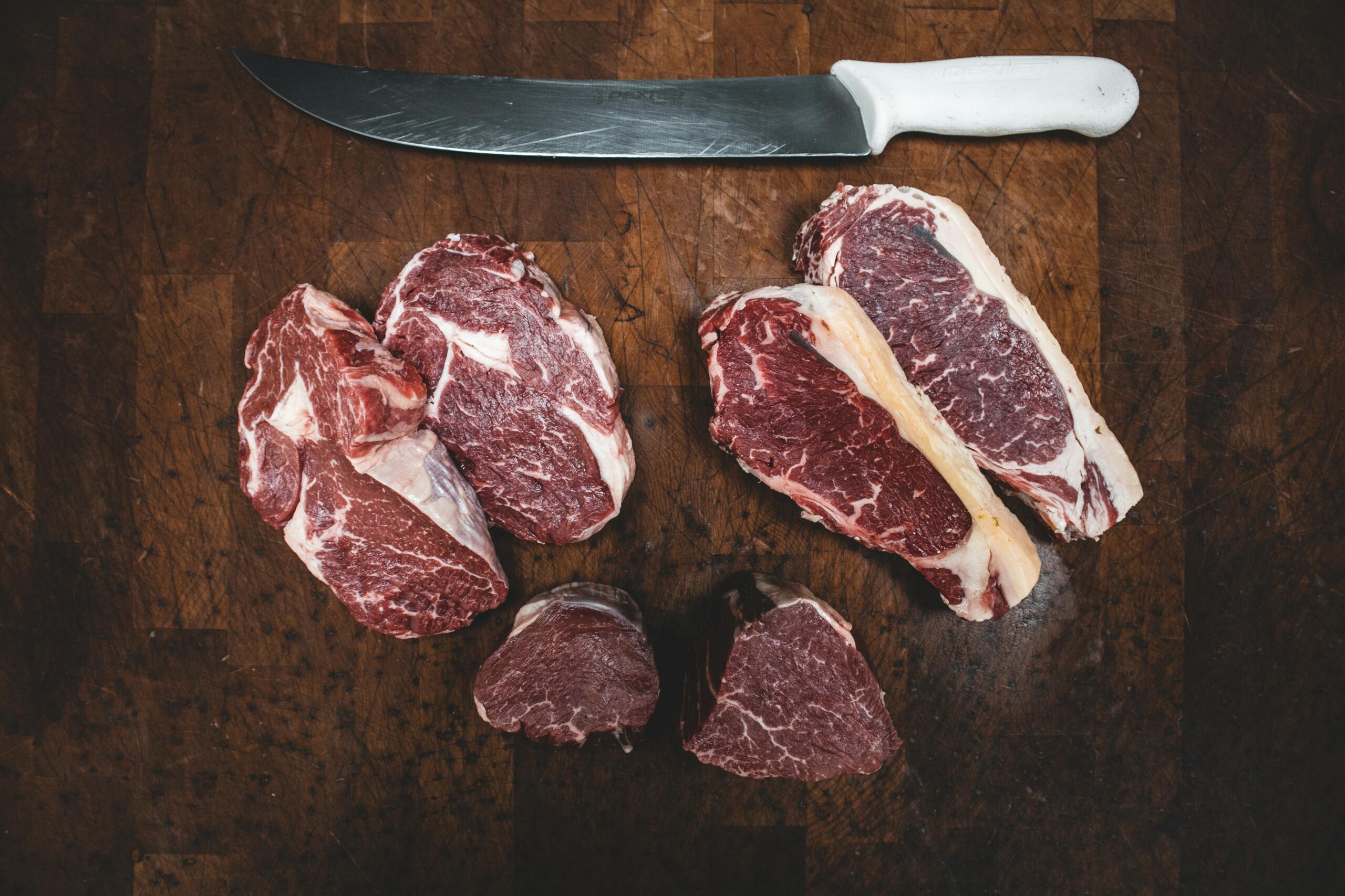 red meat cuts placed on wooden surface near large knife