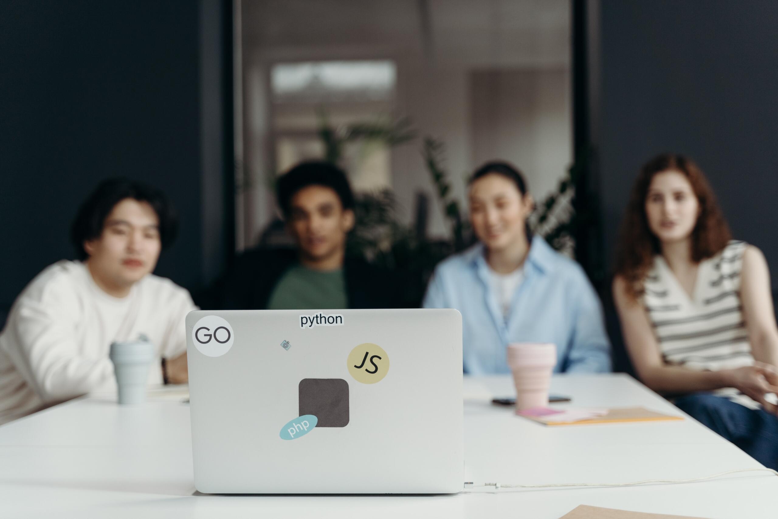 four people sitting around boardroom table looking at the same laptop screen