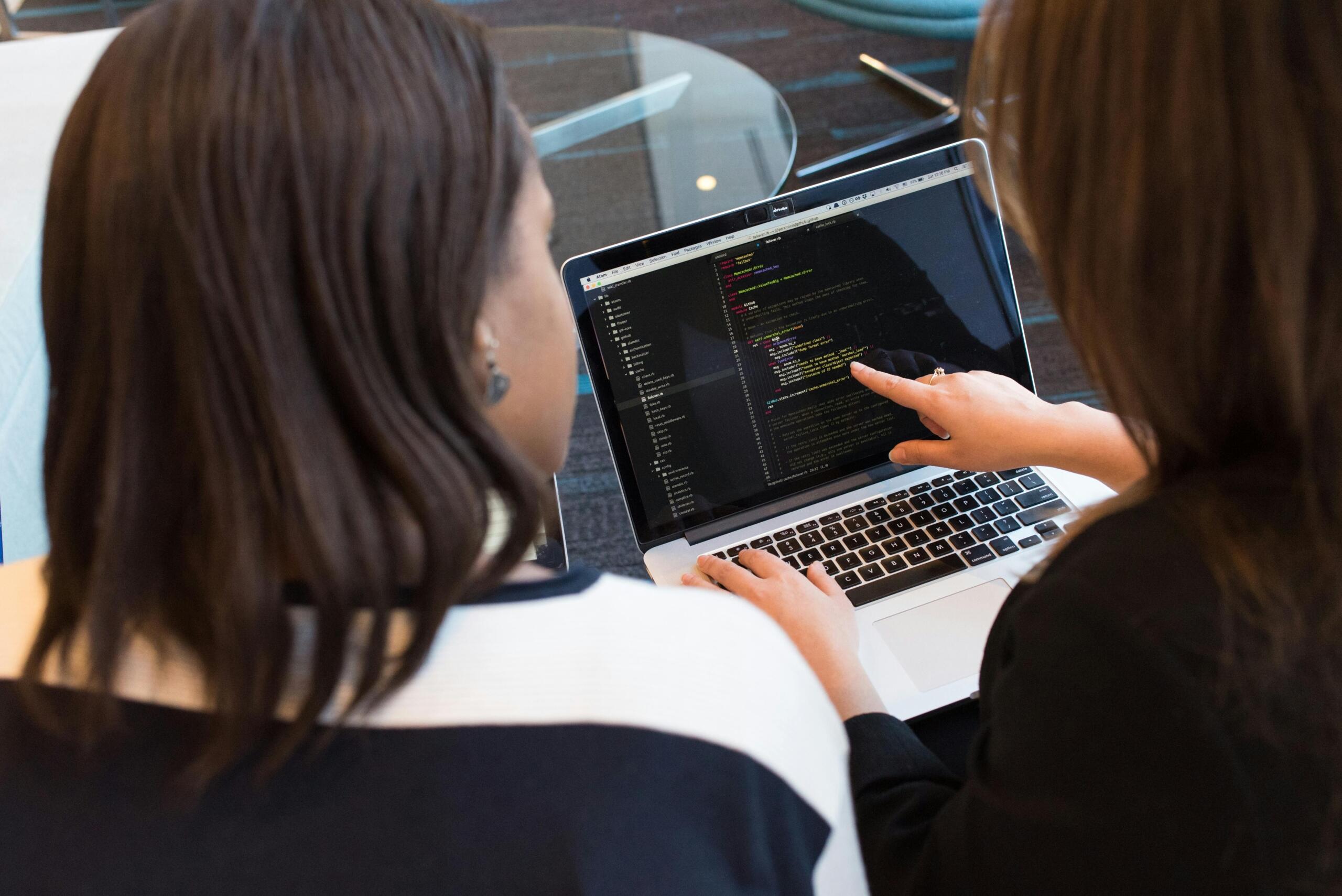 two women looking at computer code on a laptop screen