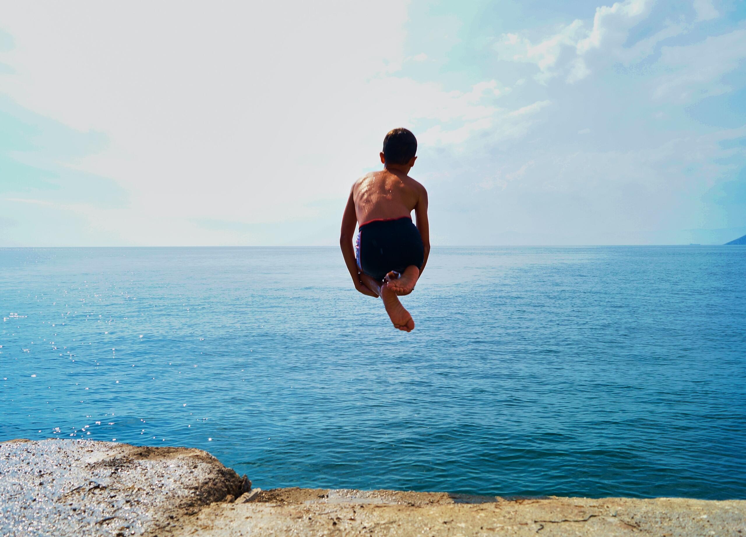 young boy jumping off concrete wall into the ocean