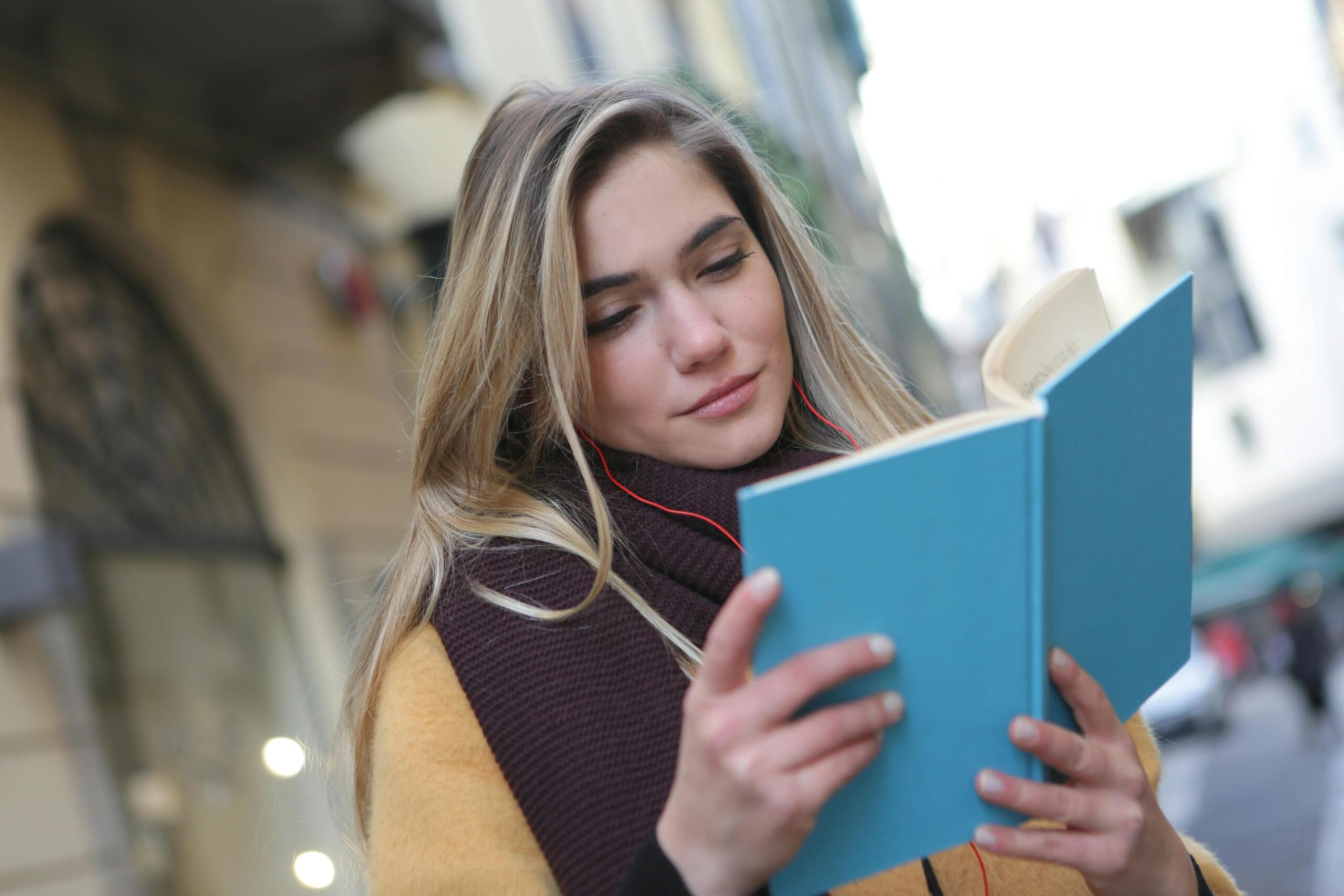 woman standing in the street in a city reading a blue book