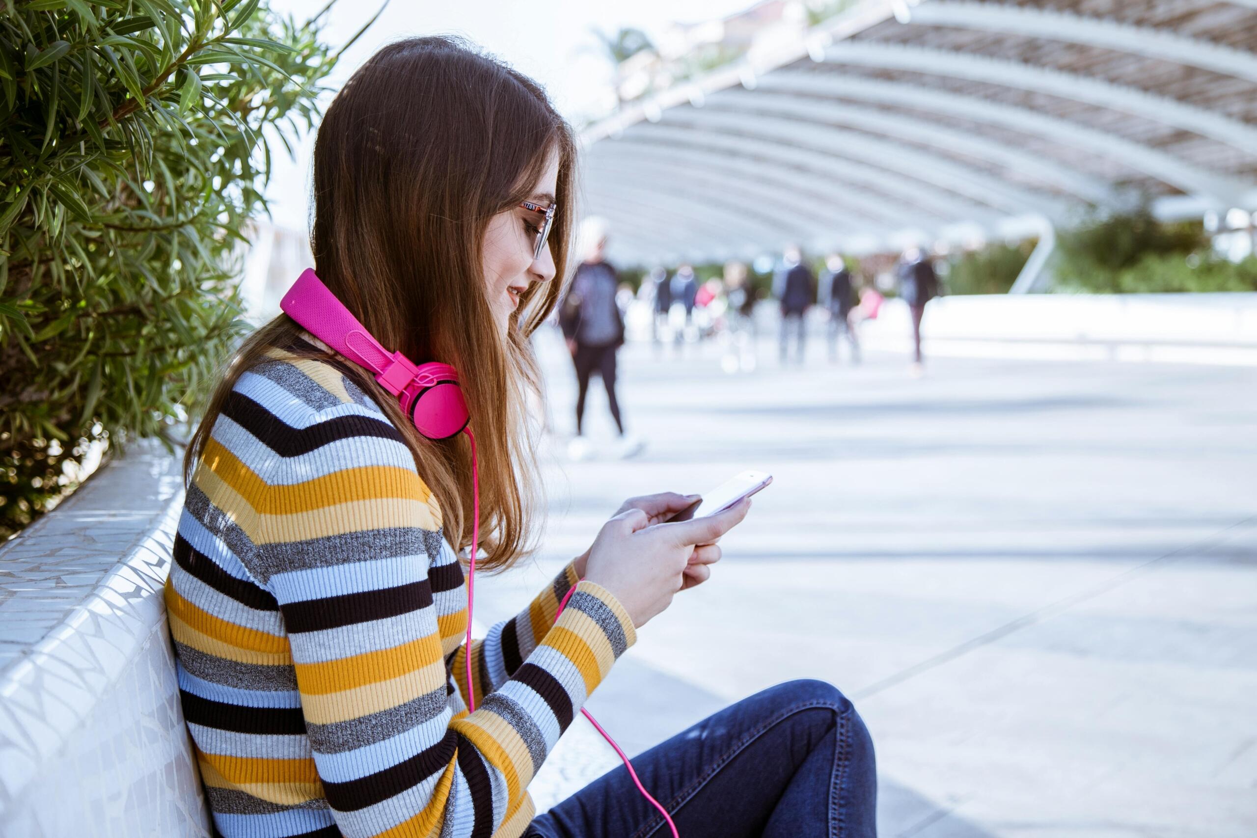 woman wearing bright pink headphones and typing on mobile phone
