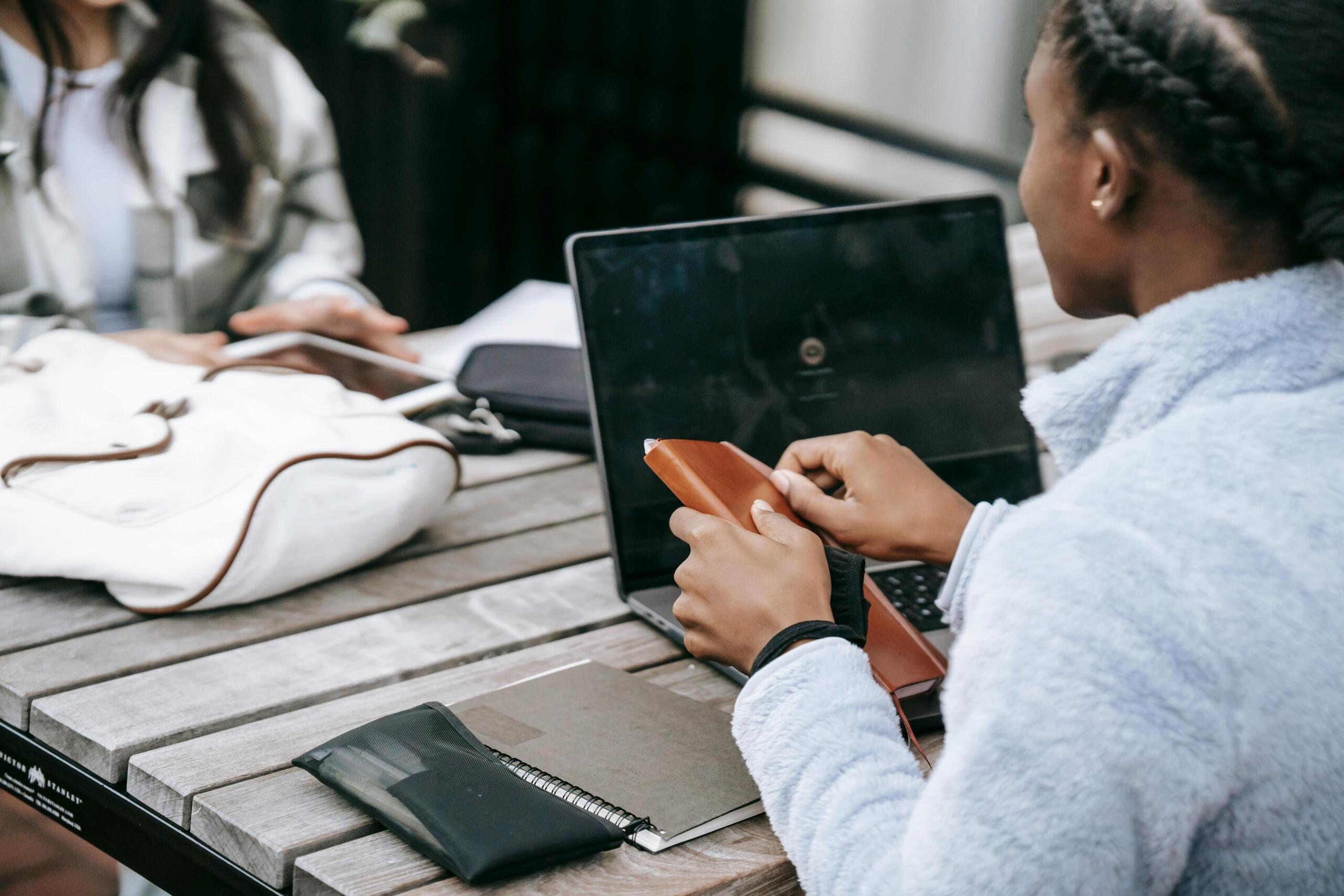 two people sitting at outdoor table using laptop and tablet
