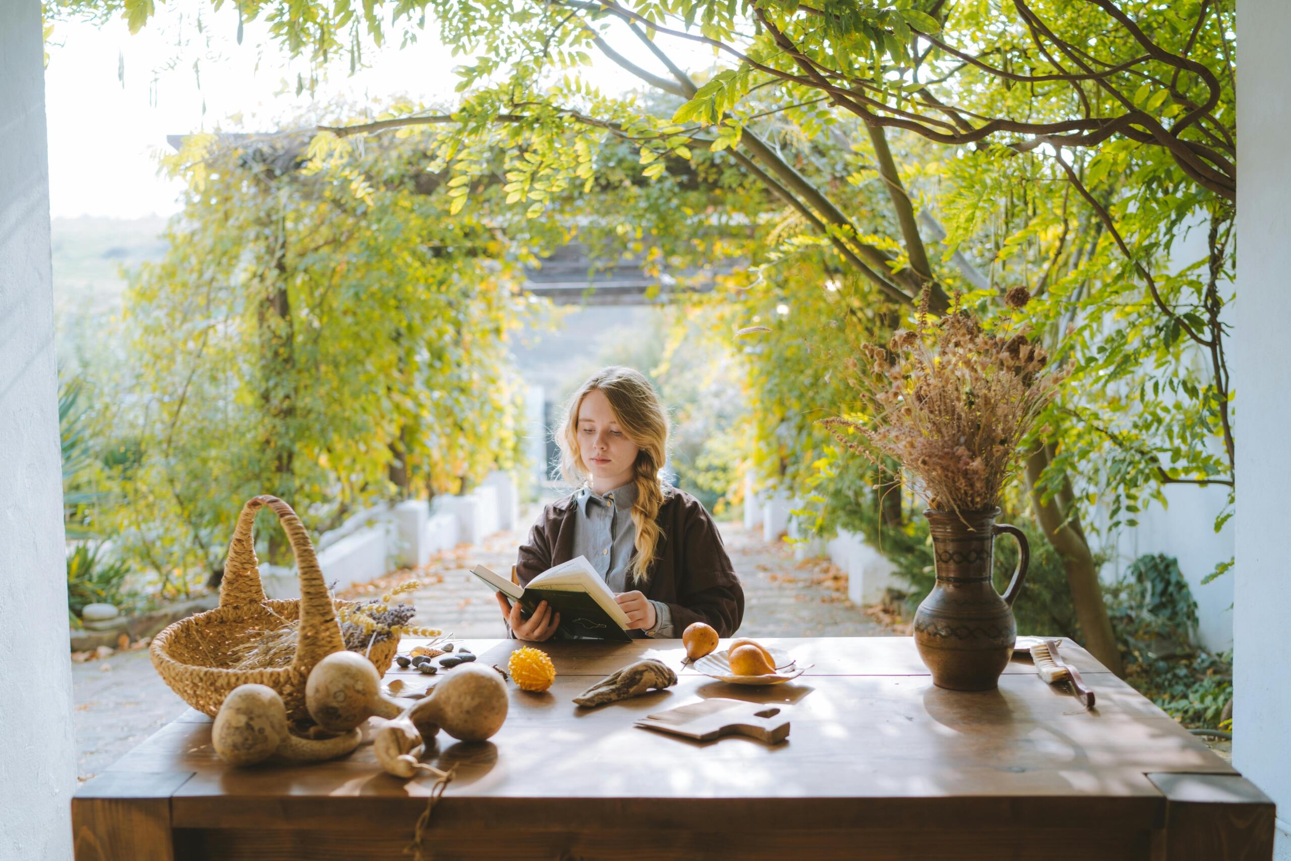 person sitting at a table under tree pergola paging through a book