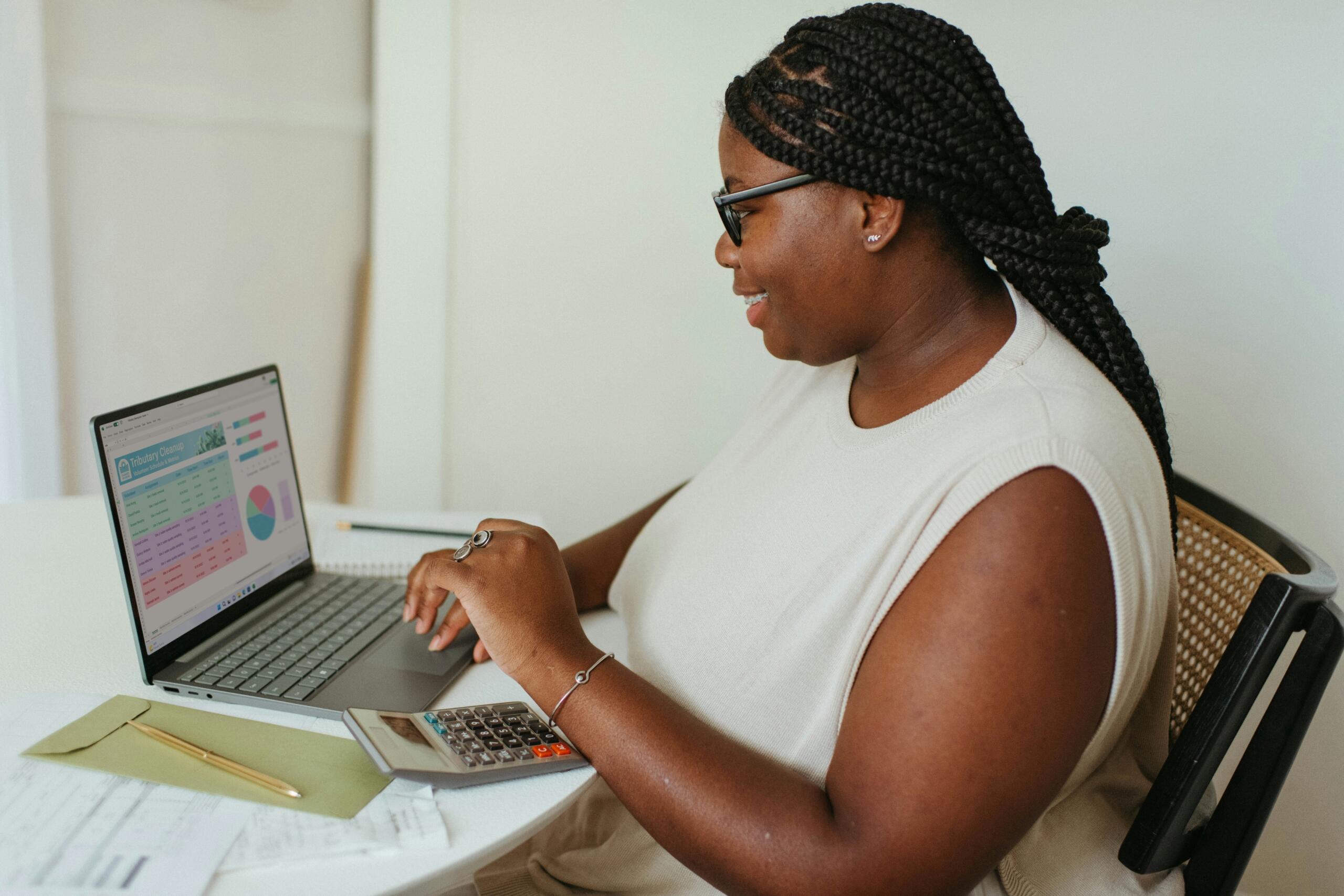 woman sitting at desk looking at data on laptop and calculator