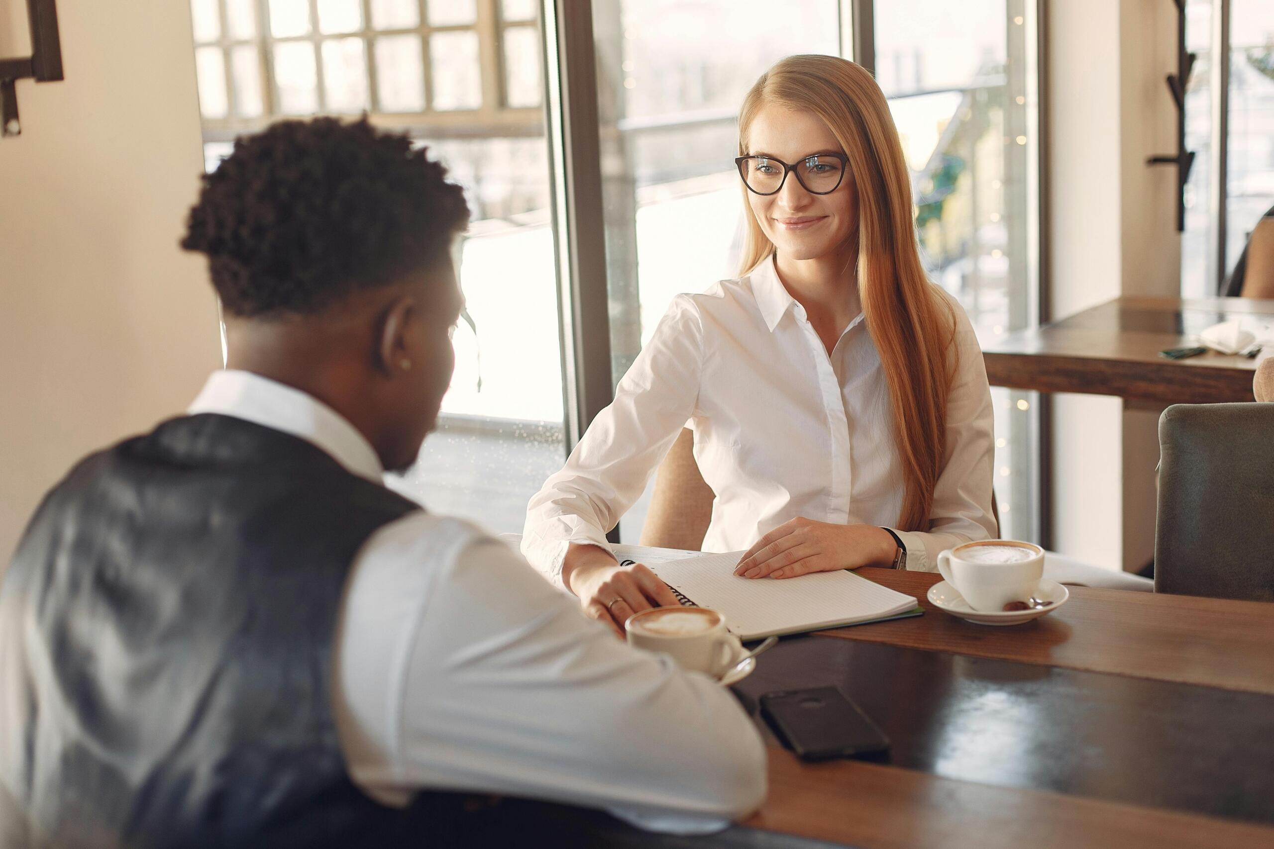 man and woman sitting across a table from each other drinking cappuccinos
