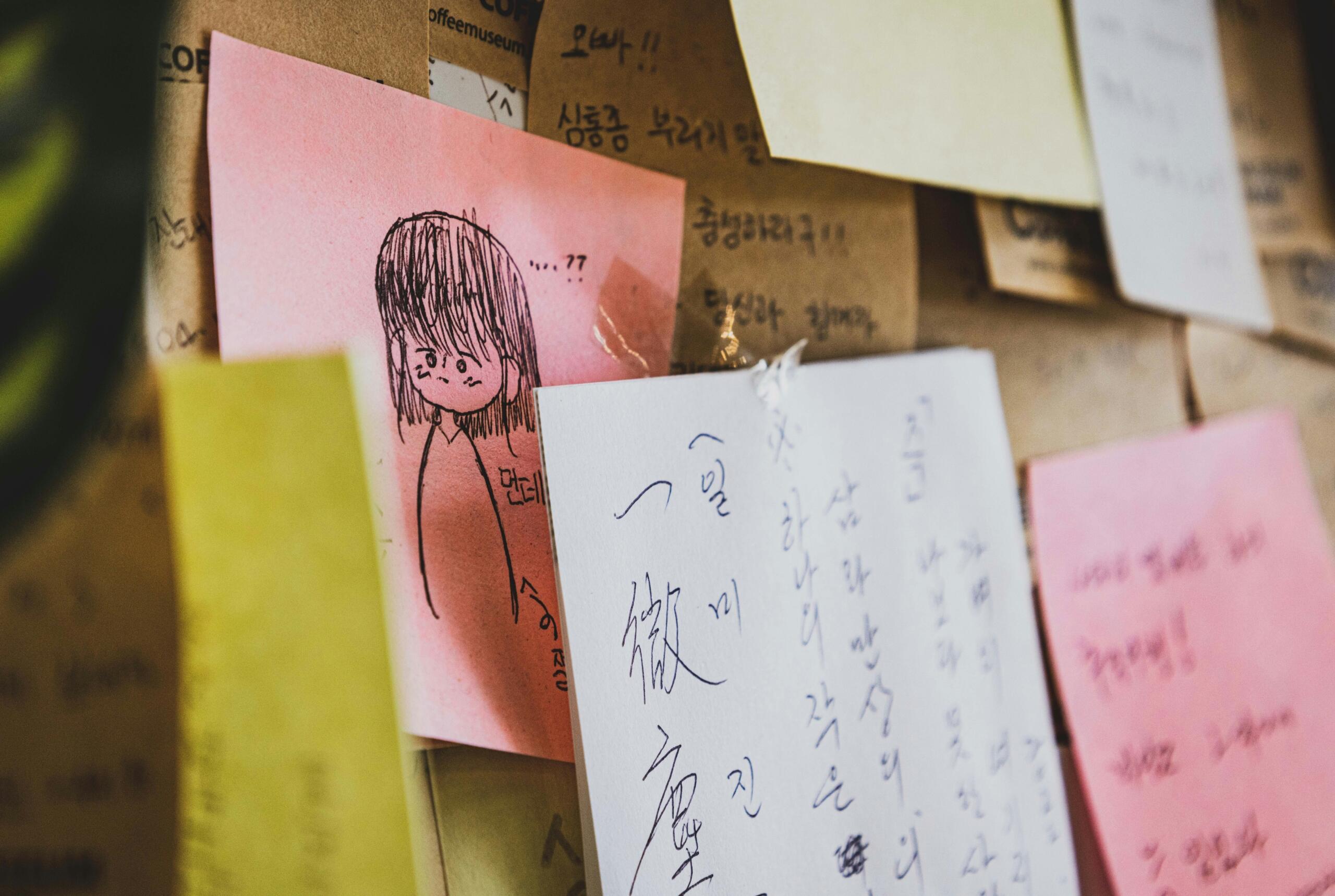 pieces of paper containing Korean Hangul characters pinned to a noticeboard alongside sketches