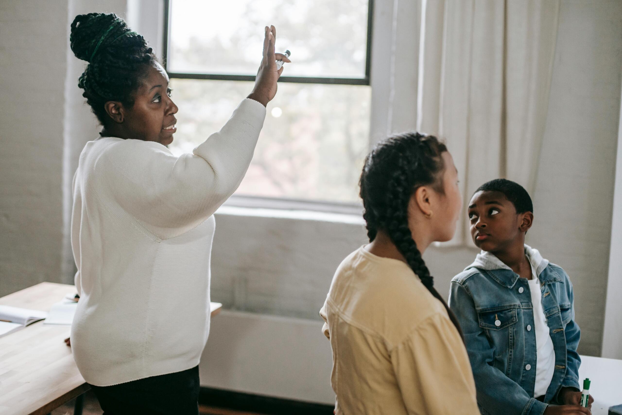 teacher standing near students gesturing in the air with her hand