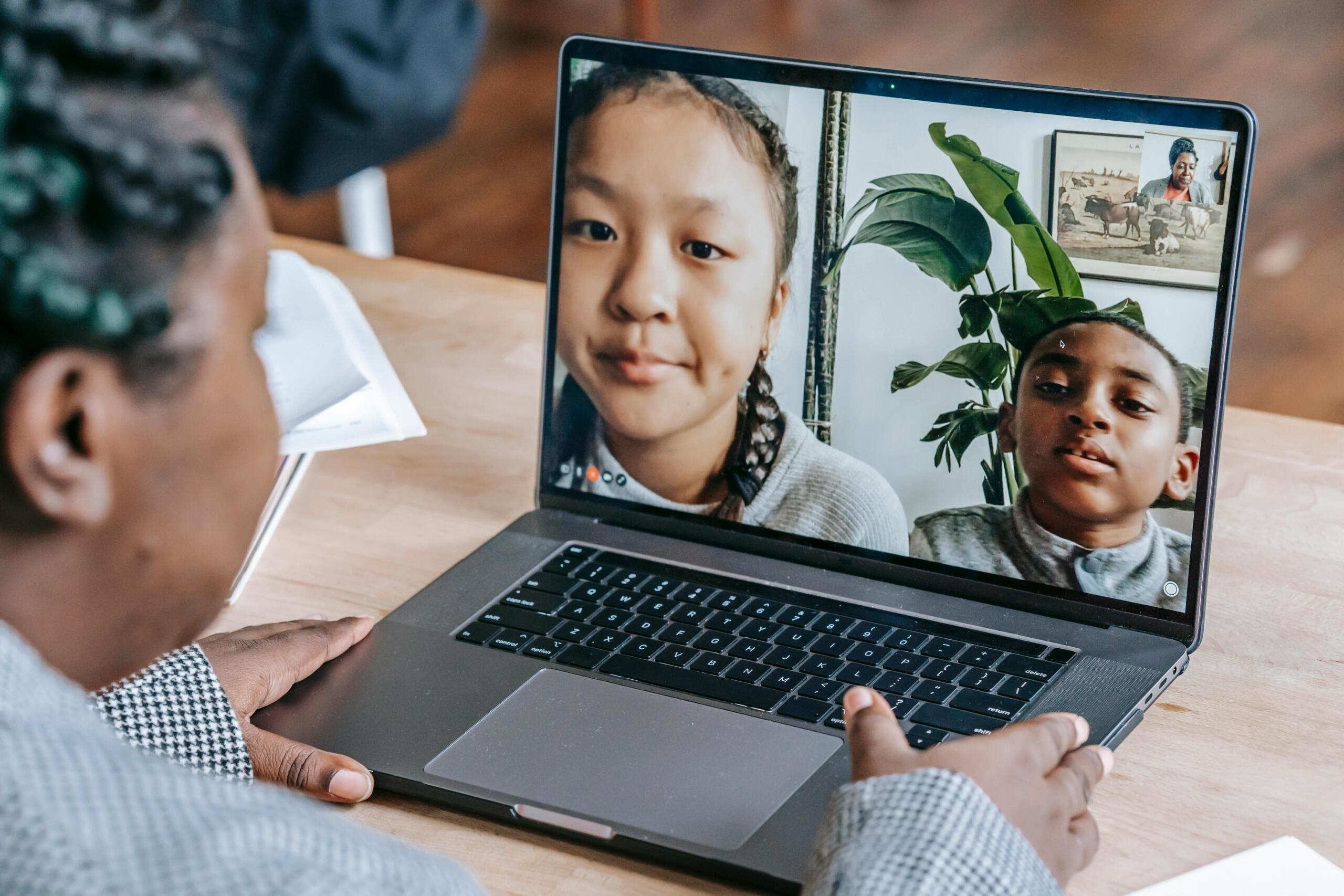 teacher using laptop to give online class to two students whose faces appear on her screen