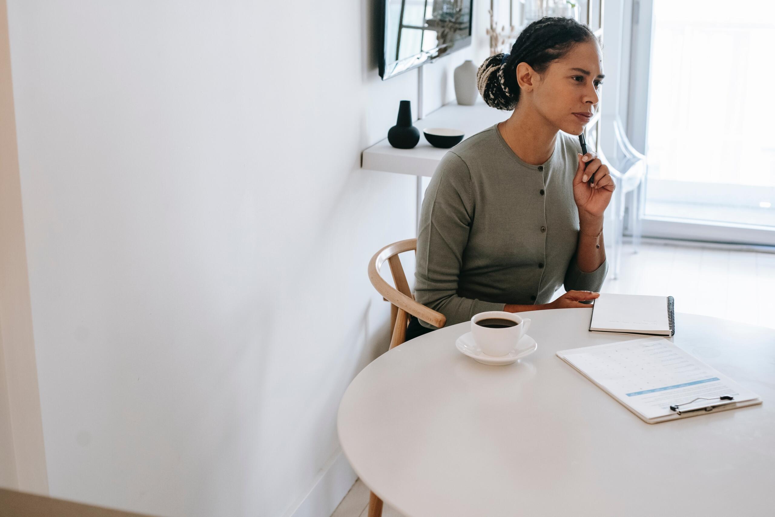 woman seated a table with a cup of coffee, a notepad and a clipboard in front of her